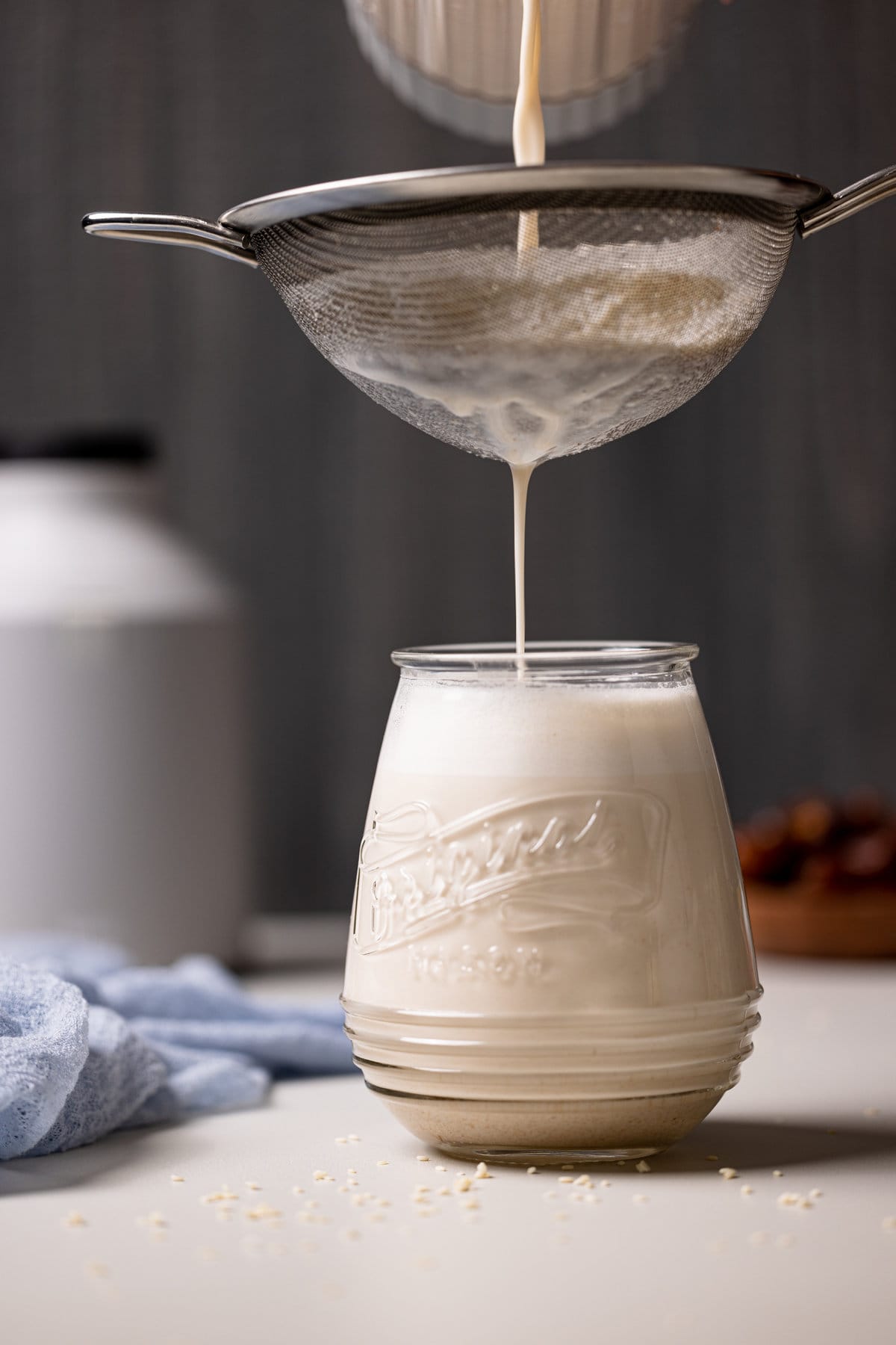 Creamy Vanilla Sesame Milk pouring through a sieve into a glass