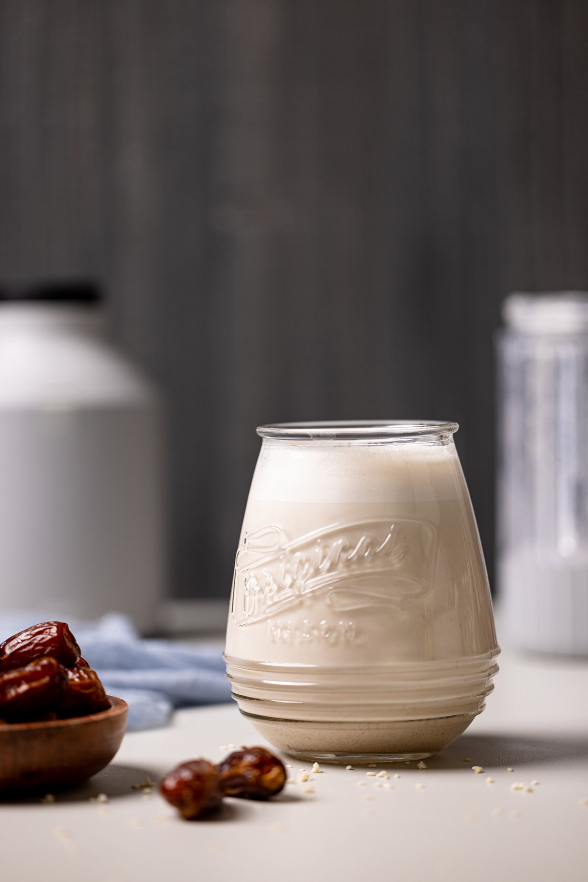 Glass of Creamy Vanilla Sesame Milk next to a bowl of dates