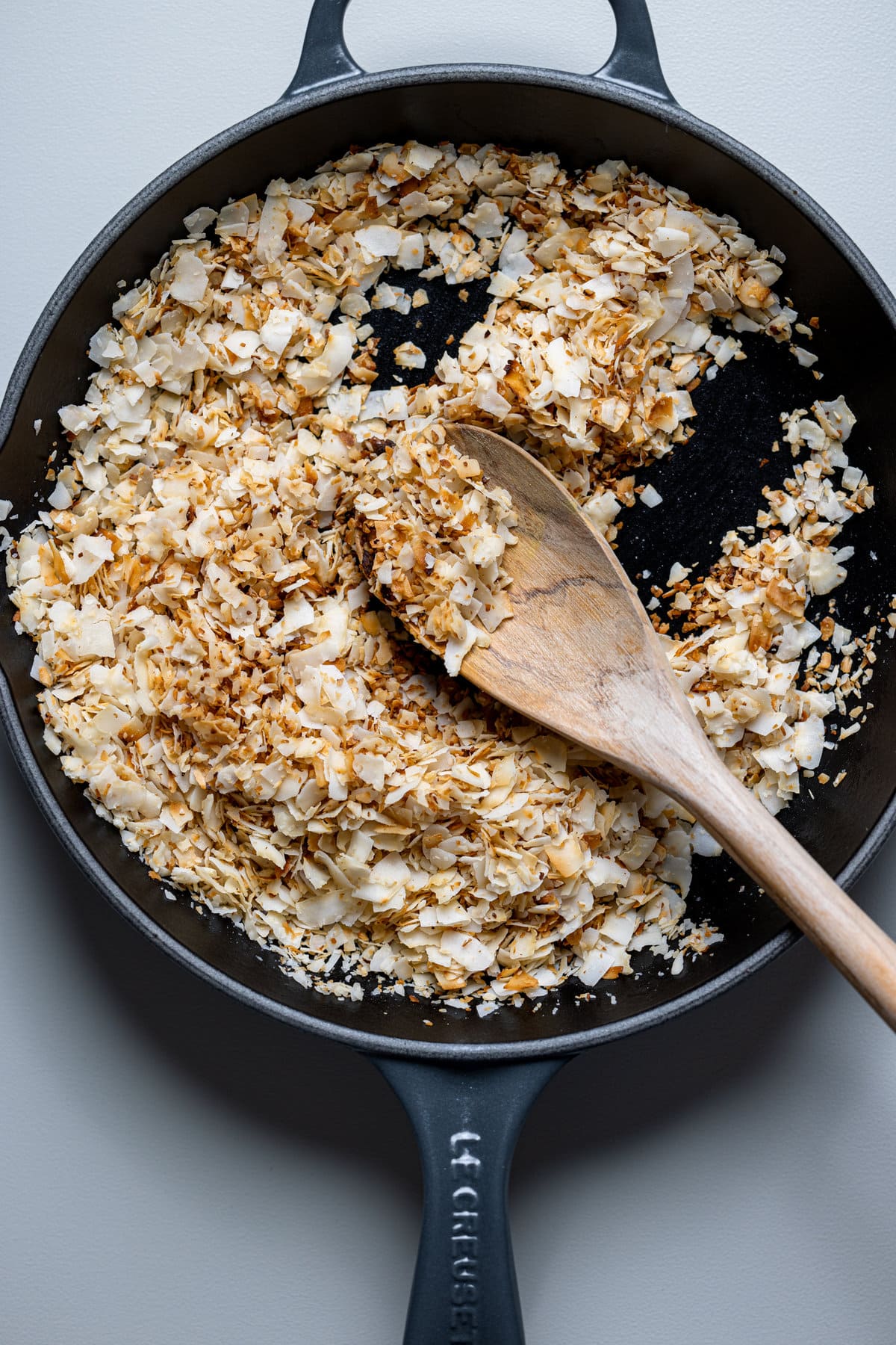 Wooden spoon stirring a skillet of Toasted Coconut 