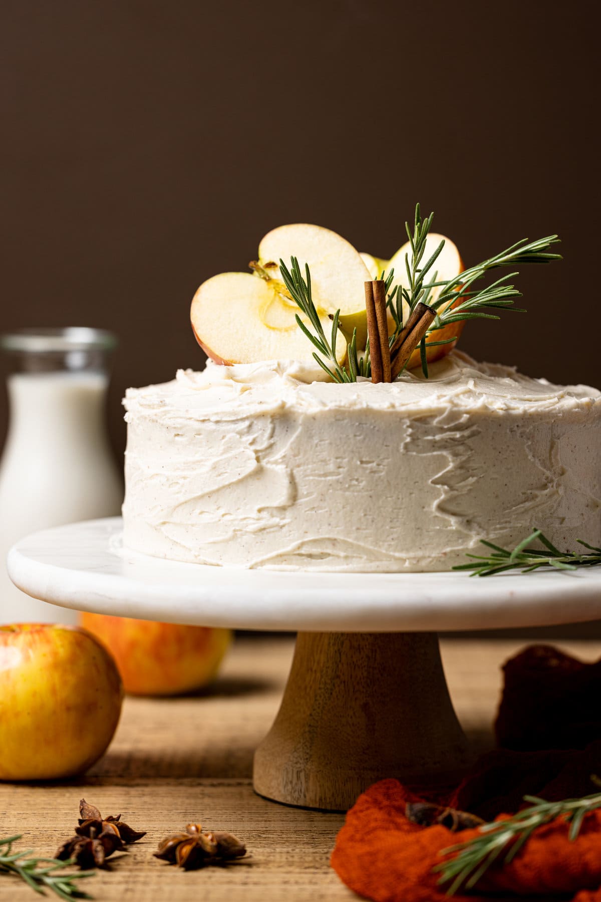 Apple Cider Cake with Cinnamon Maple Buttercream topped with cinnamon sticks, rosemary, and apple slices