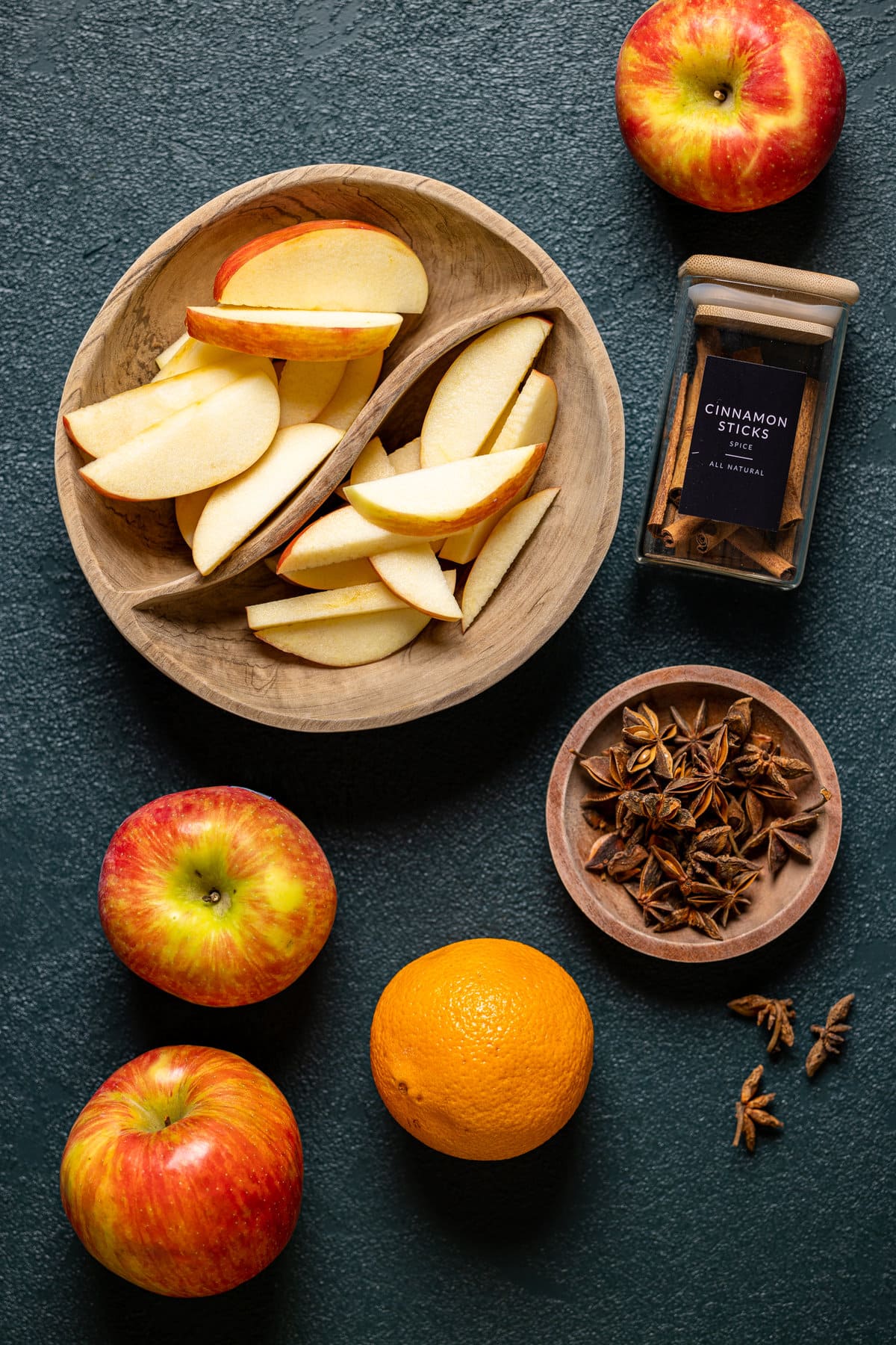 Ingredients for an Apple Cider Mocktail including cinnamon sticks, oranges, and apples