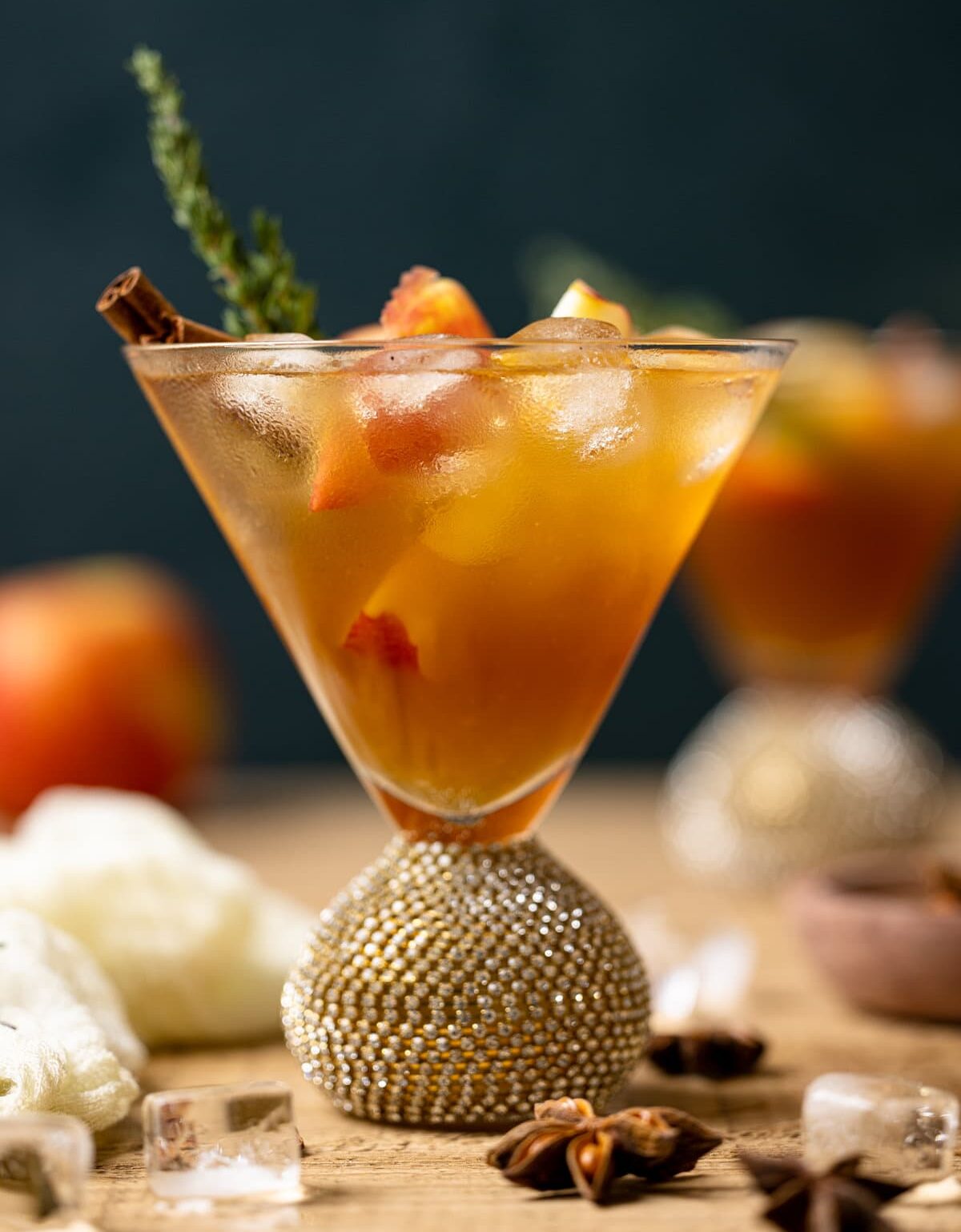 Closeup of an Apple Cider Mocktail in a jeweled cocktail glass with ice and a cinnamon stick