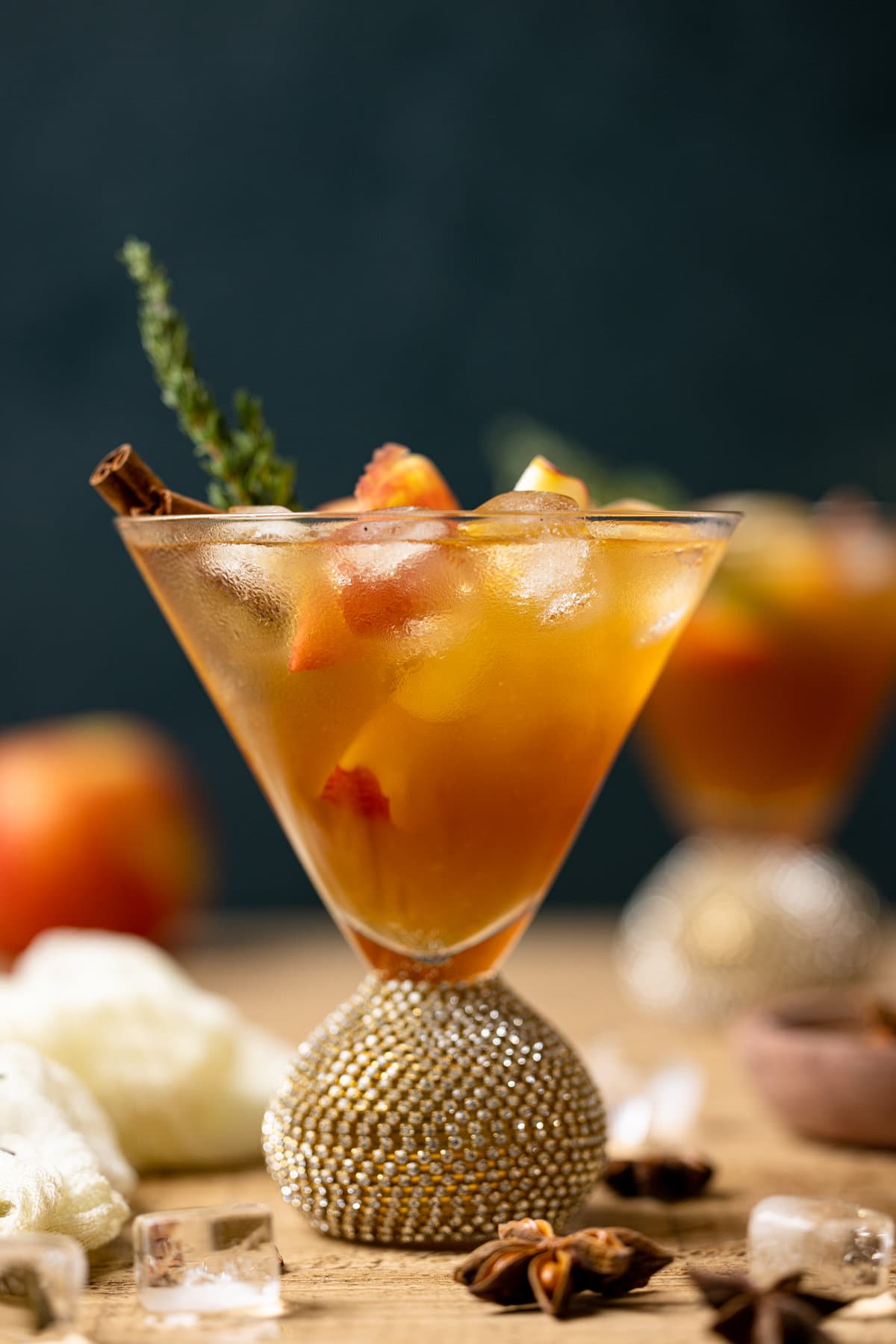 Closeup of an Apple Cider Mocktail in a jeweled cocktail glass with ice and a cinnamon stick