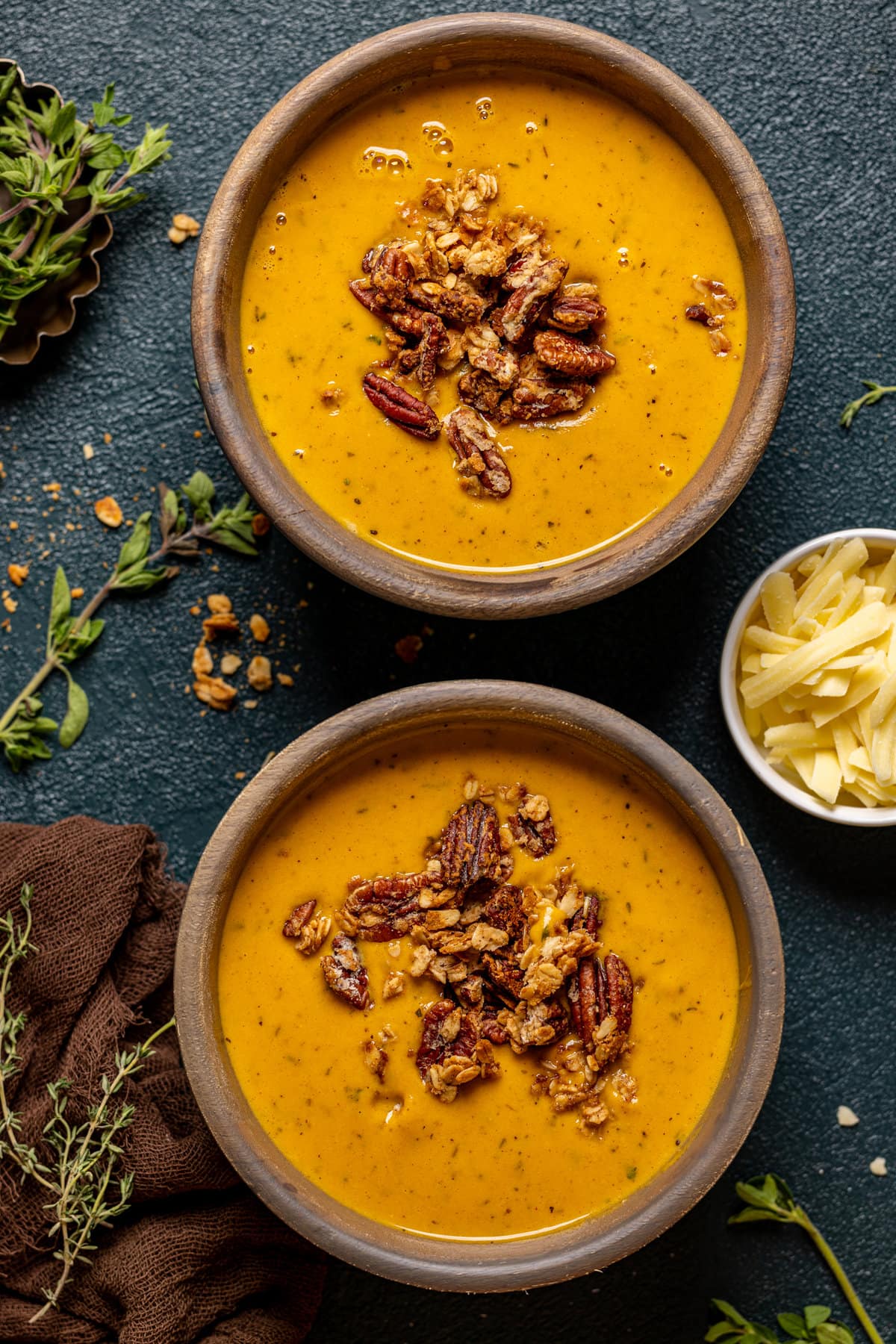 Overhead shot of two bowls of Apple Cheddar Sweet Potato Soup next to a bowl of cheese