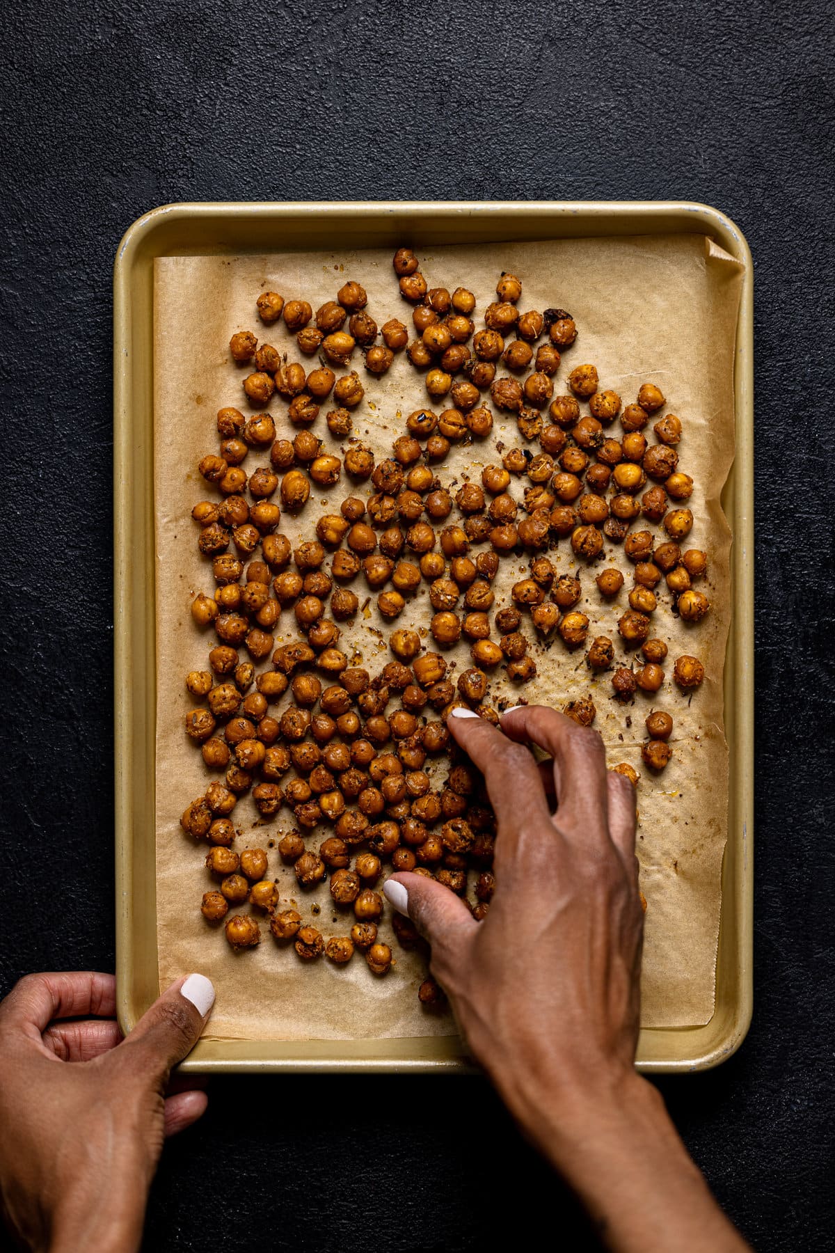 Hand grabbing some roasted Chickpeas off of a baking sheet