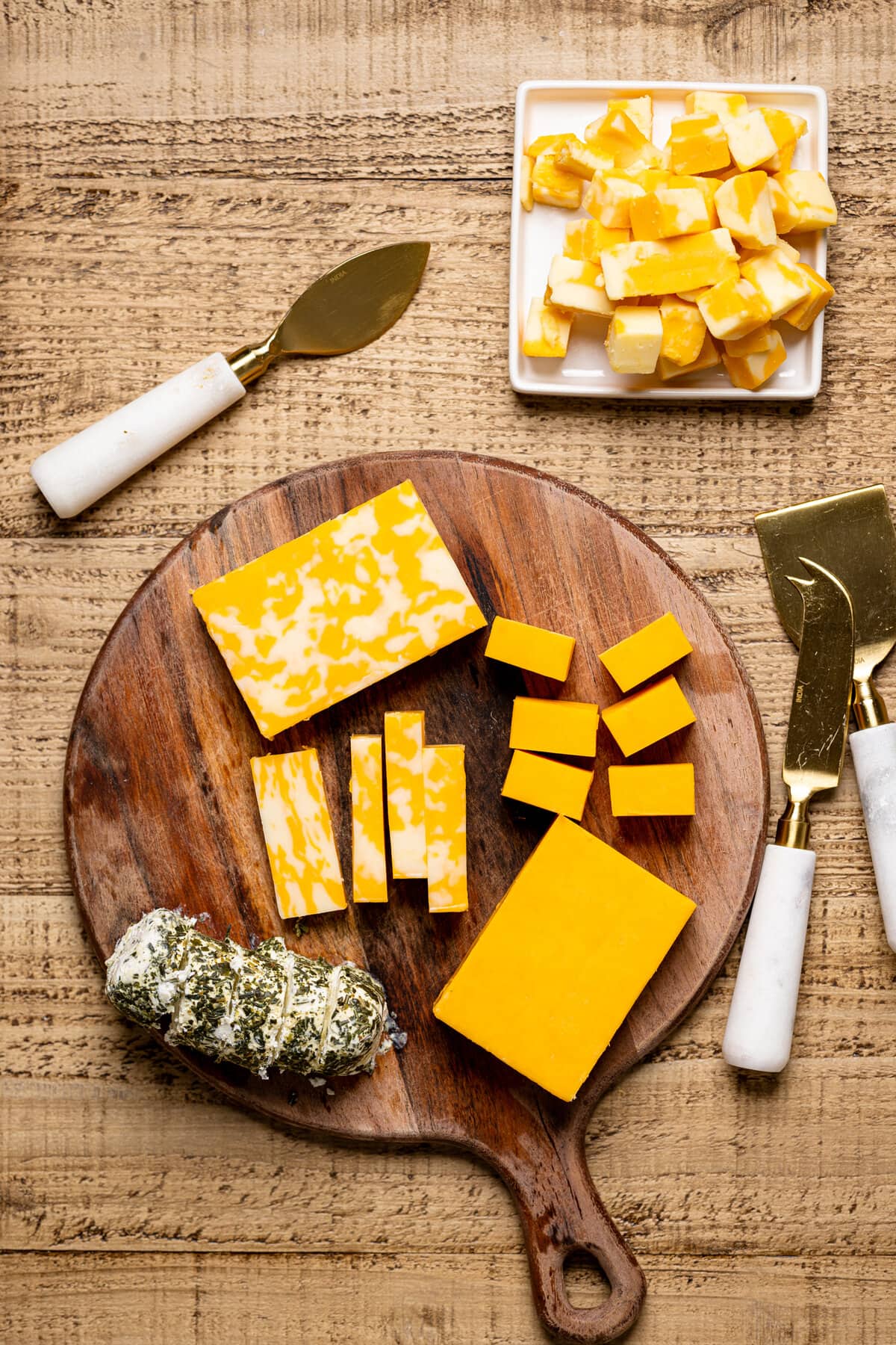 Three cheese in various stages of being cut on a wooden cutting board