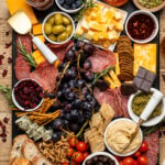 Overhead shot of a colorful and extensive Charcuterie Board including black grapes, green olives, crackers, cheeses, and dips