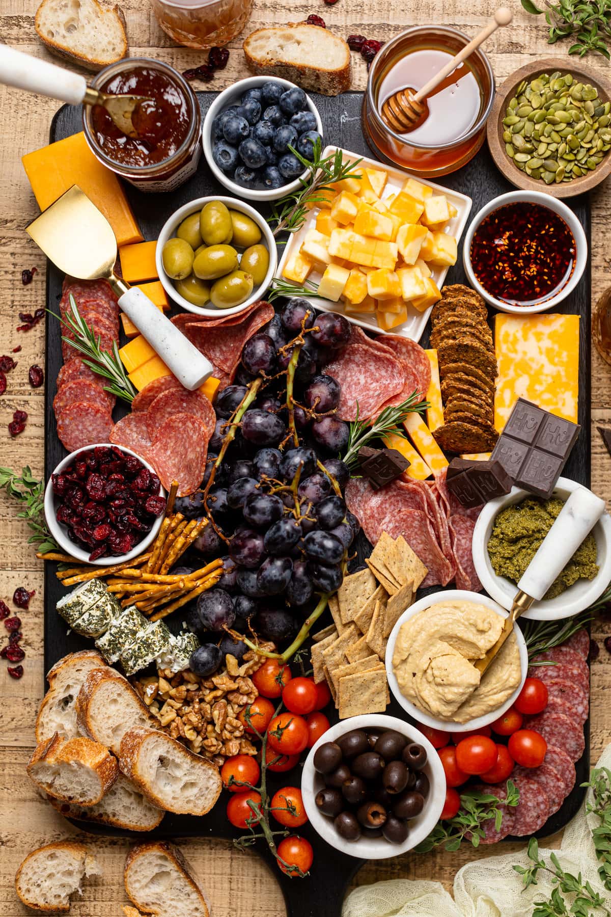 Overhead shot of a colorful and extensive Charcuterie Board including black grapes, green olives, crackers, cheeses, and dips