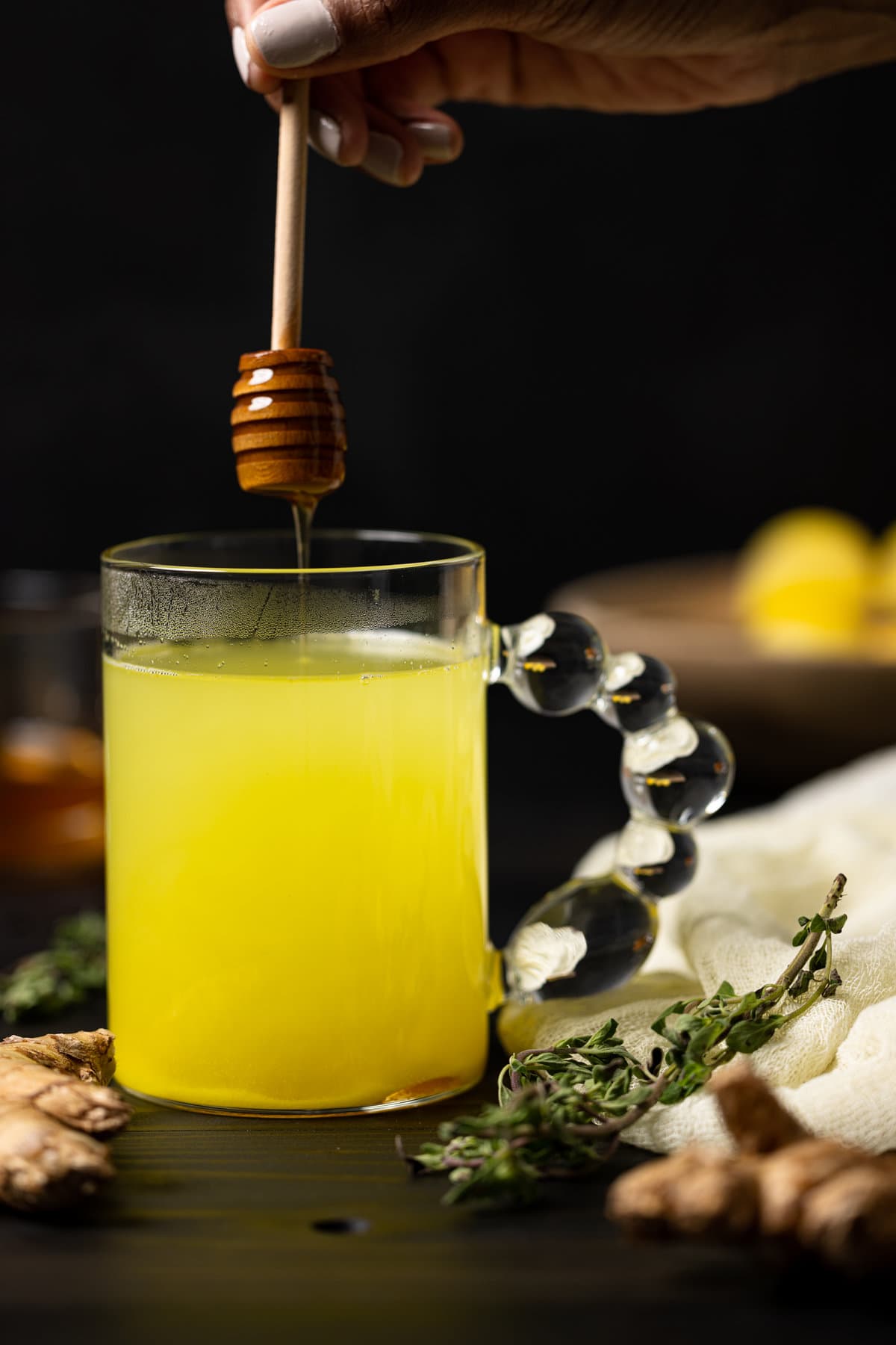 Honey drizzling into a glass of Citrus Ginger Turmeric Ice Cubes with Tea