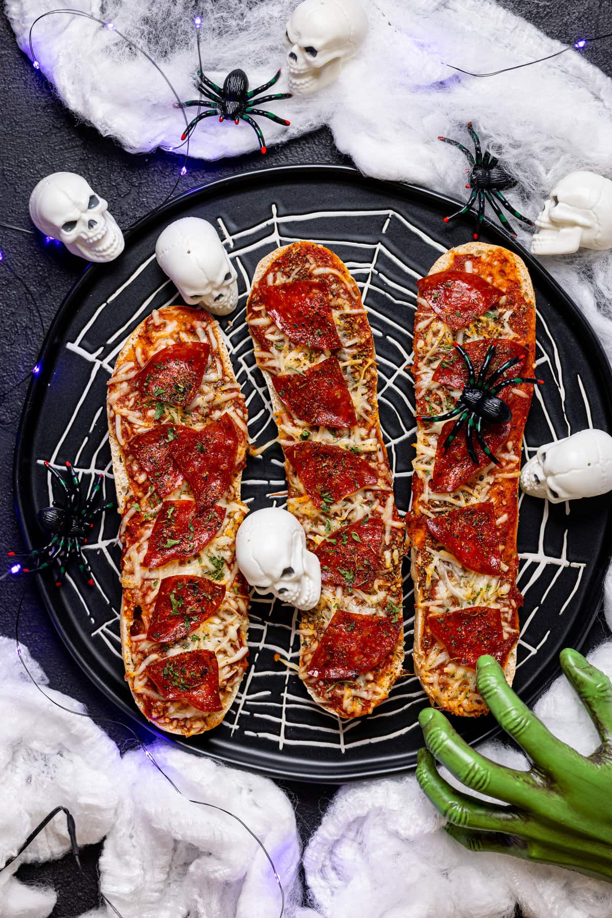 Three Spooky French Bread Pepperoni Pizzas on a spider-web plate with mini skulls, spiders, and a green hand