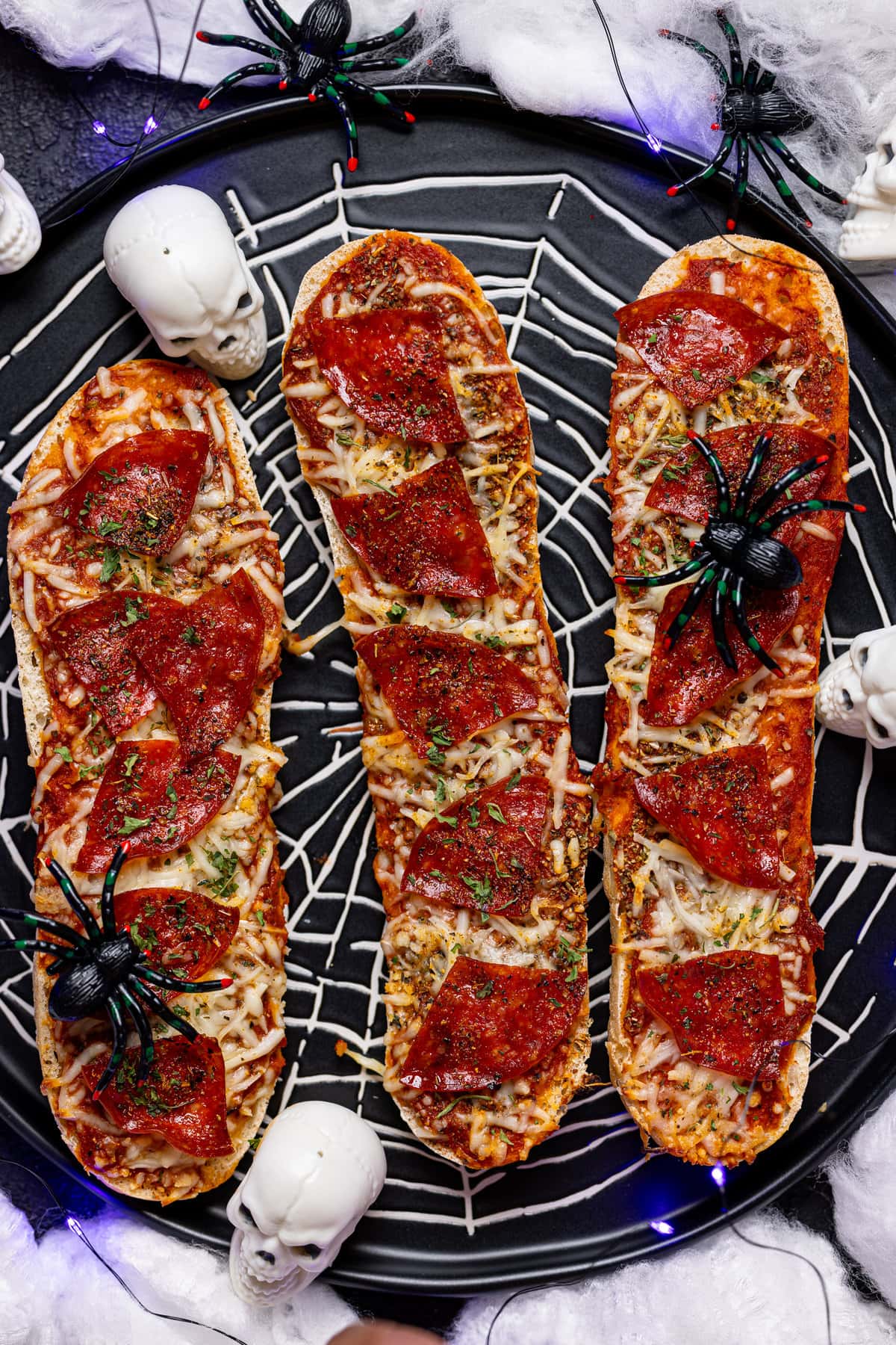 Spider-web plate with three Spooky French Bread Pepperoni Pizzas decorated with mini skulls and spiders