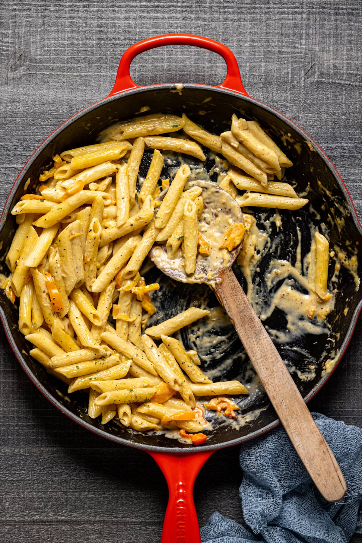 Wooden spoon scooping Creamy Jamaican Rasta Pasta out of a skillet
