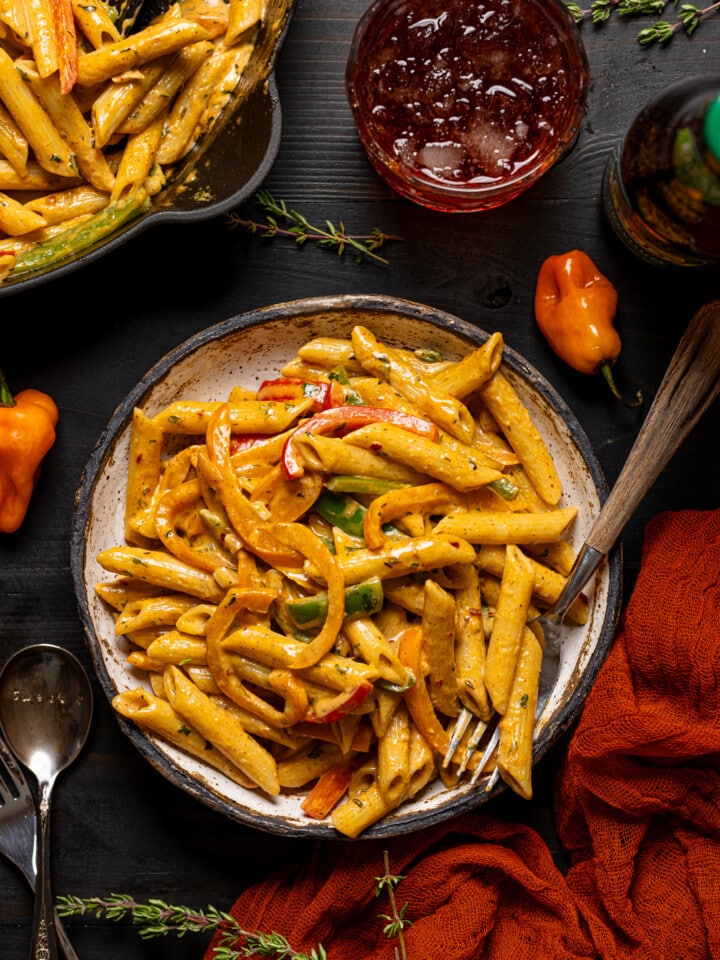 Pasta in a white low bowl with a drink and skillet full of pasta on the side.