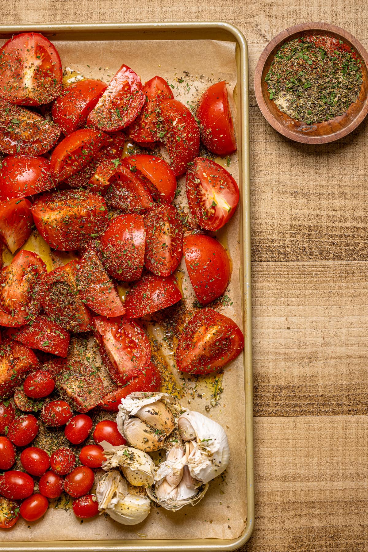 Seasoned tomatoes and garlic bulbs on a baking sheet