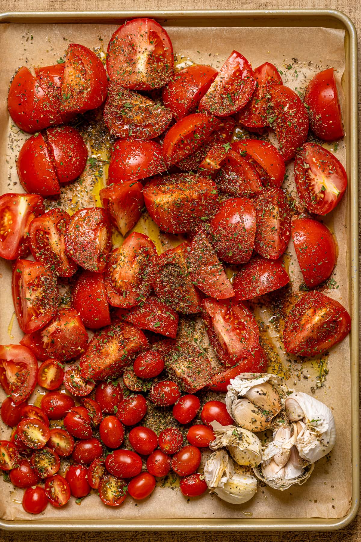Seasoned tomatoes and garlic bulbs on a baking sheet