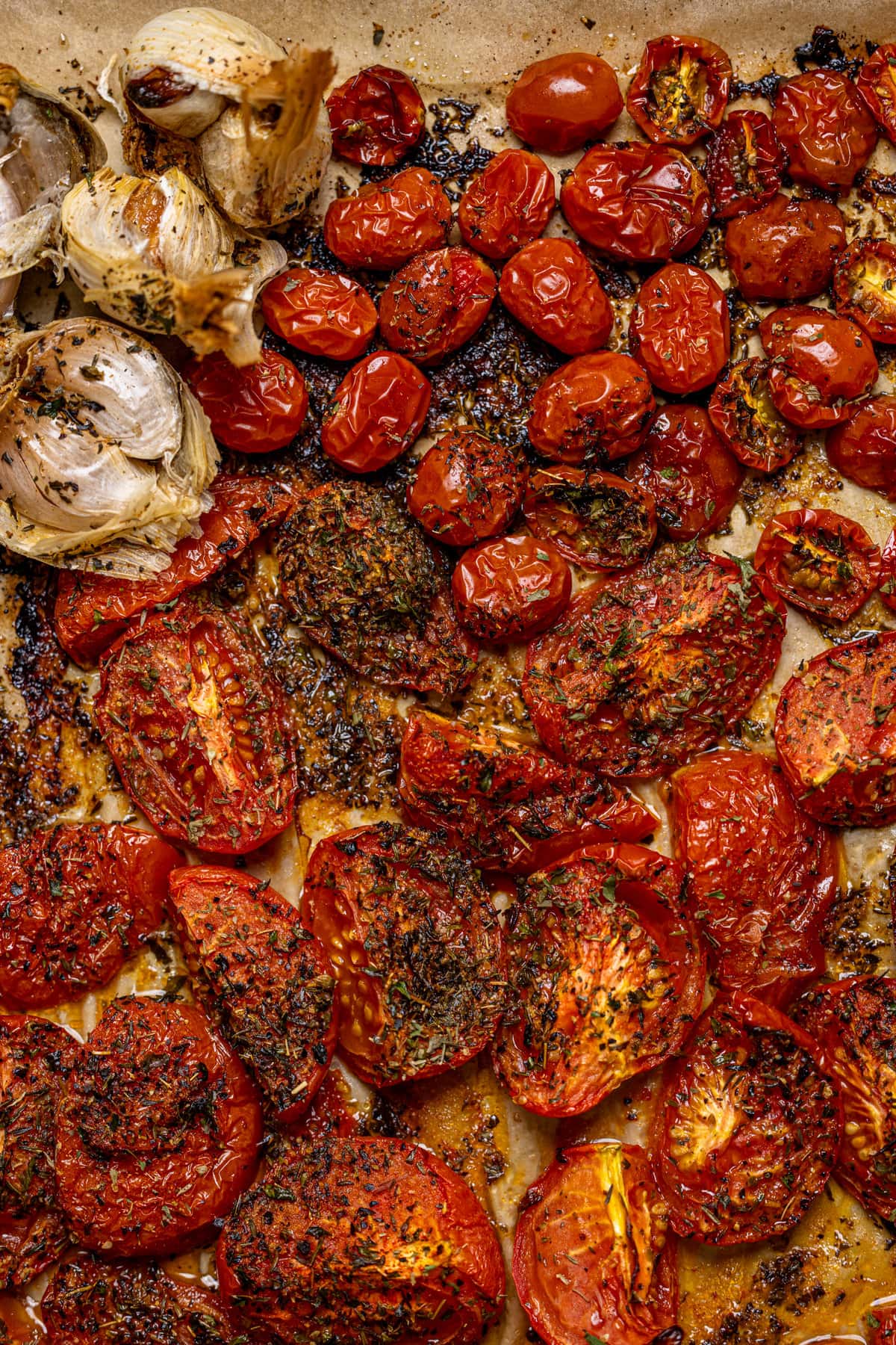 Roasted tomatoes and garlic bulbs on a baking sheet