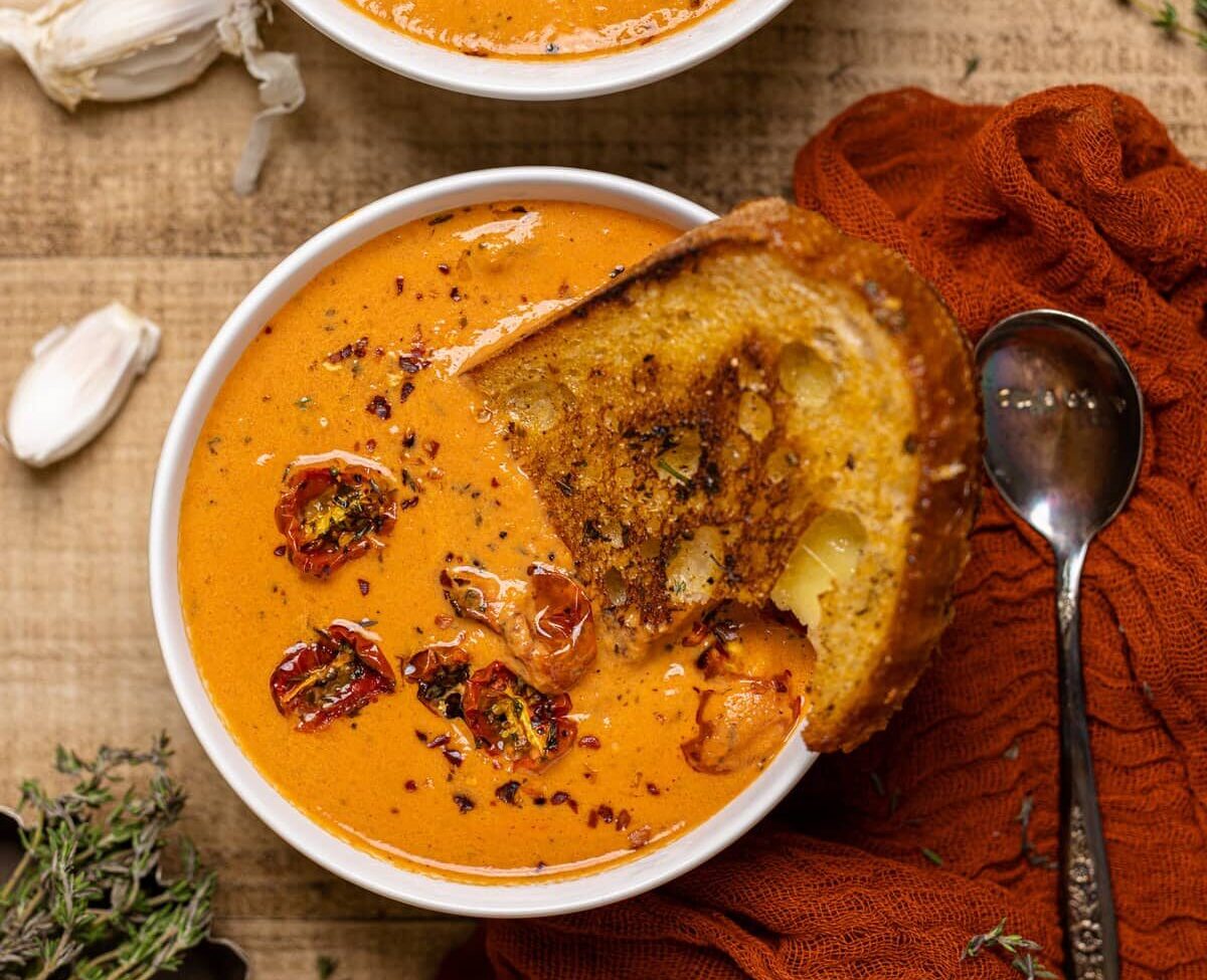 Slice of toast being dipped into a bowl of Creamy Roasted Garlic Tomato Soup