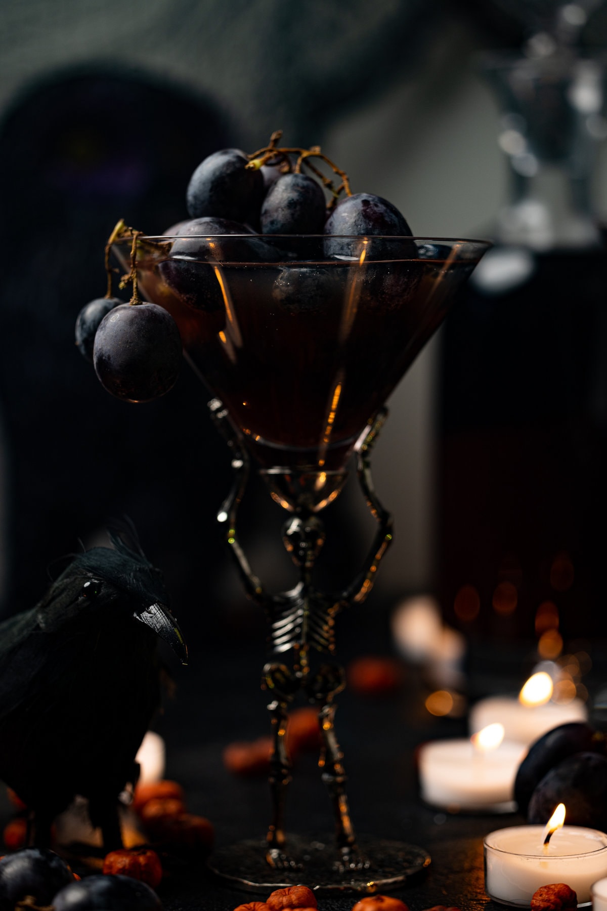 Halloween Witches Brew Mocktail in skeleton glassware overflowing with black grapes next to a black bird