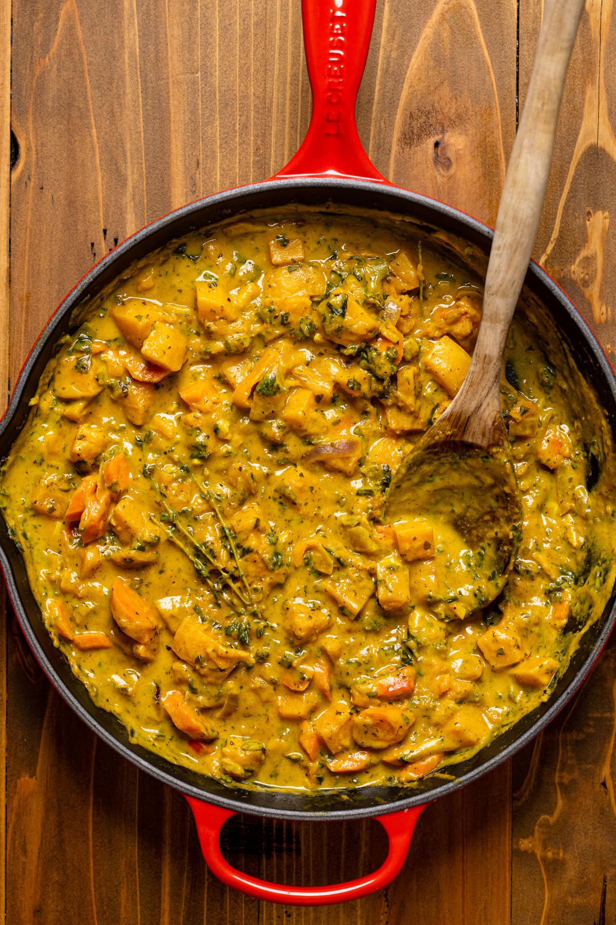Wooden spoon stirring Vegan Pumpkin Curry Butternut Squash in a skillet