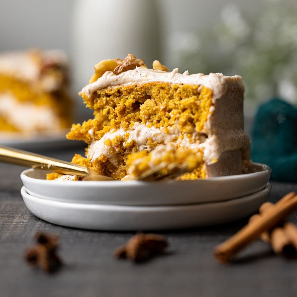 Slice of carrot cake on a stack of two plates with a fork on a grey table.