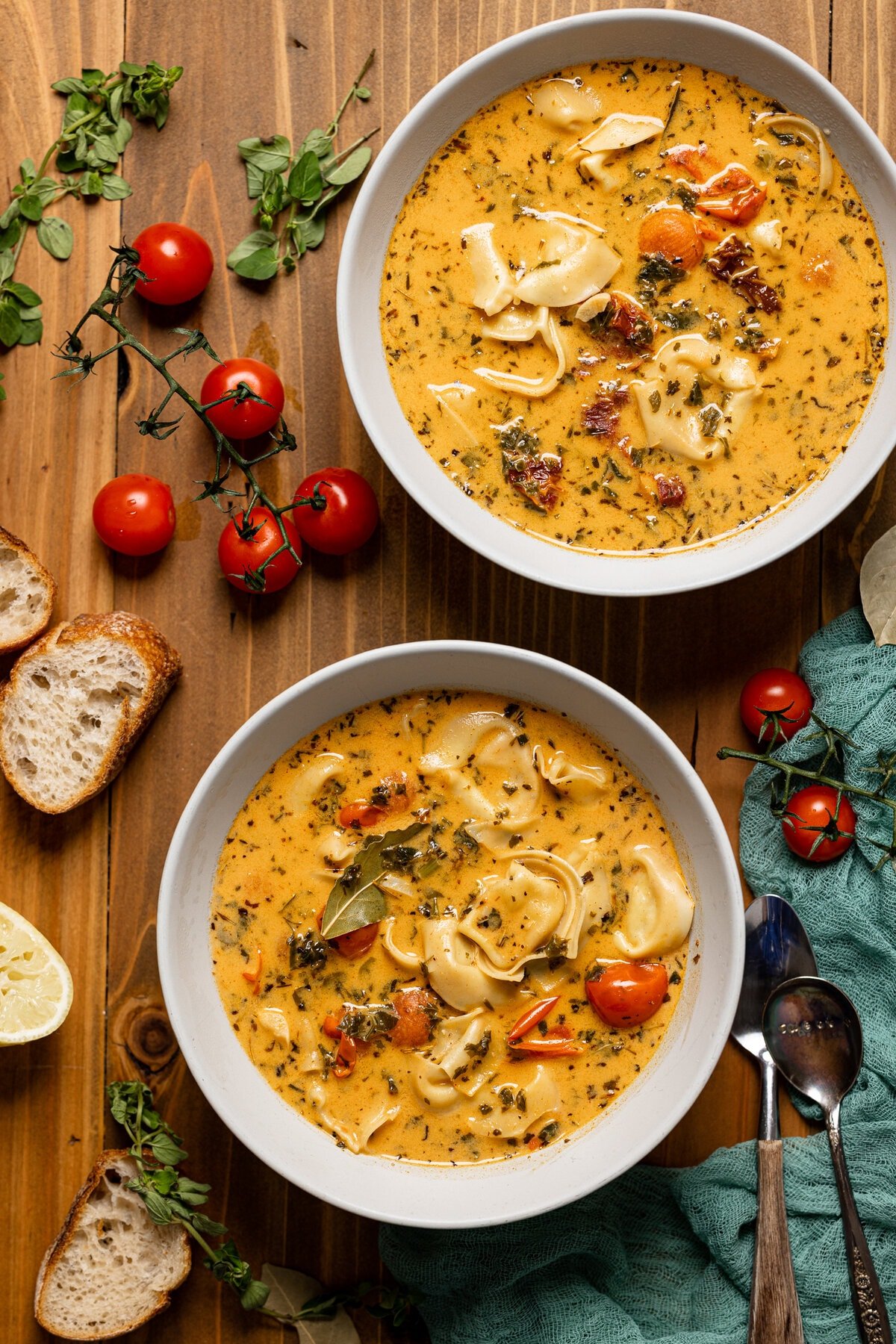 Overhead shot of two bowls of Creamy Tuscan Tortellini Soup surrounded by tomatoes and slices of bread