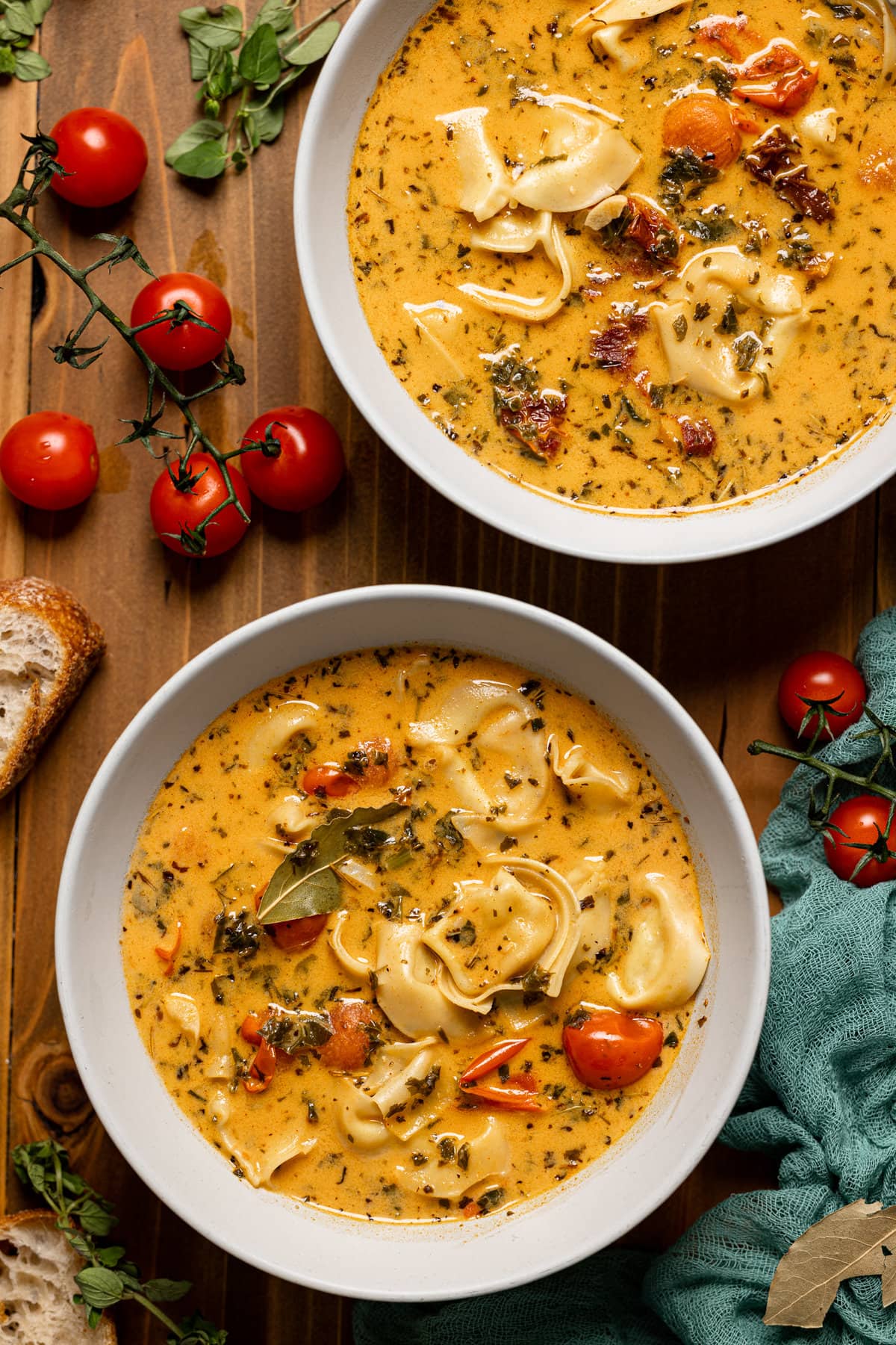 Overhead shot of two bowls of Creamy Tuscan Tortellini Soup surrounded by tomatoes and slices of bread