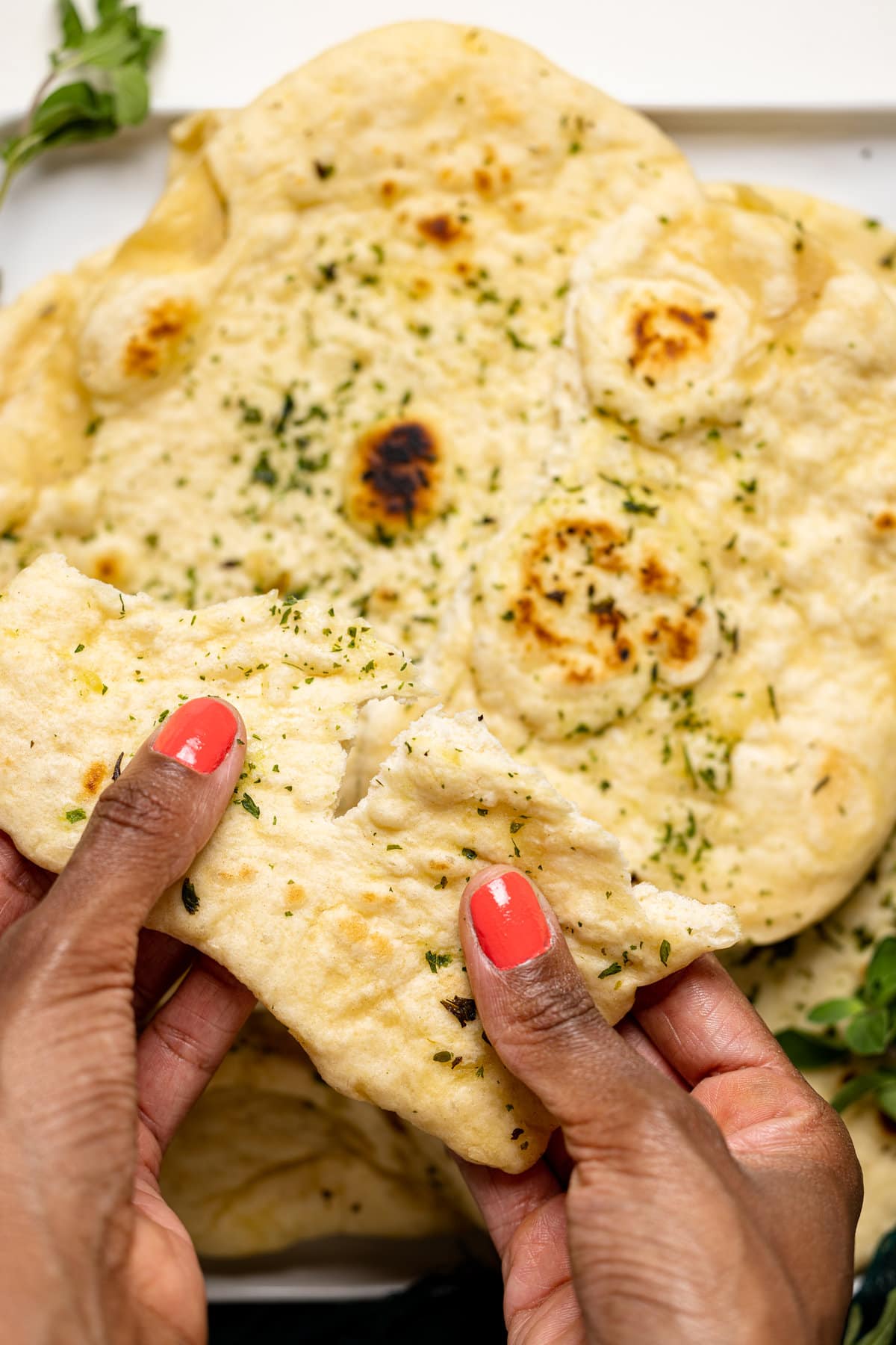 Hands tearing a piece of Vegan Garlic Naan Bread