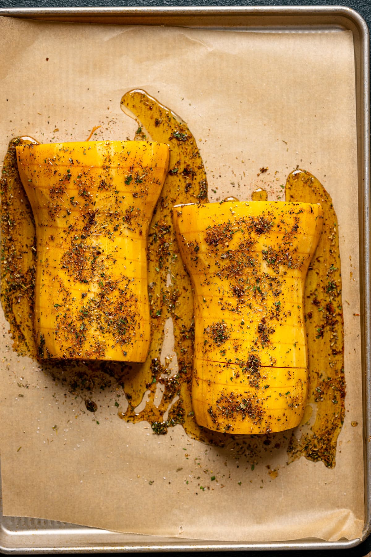 Sliced, halved, and seasoned butternut squash on a baking sheet