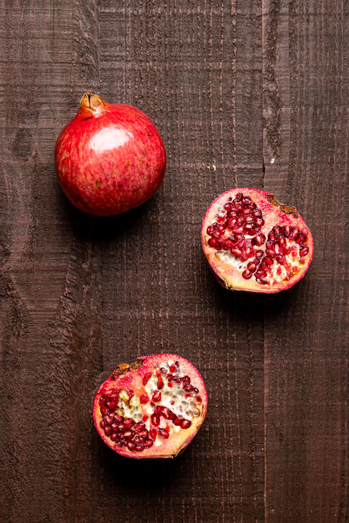 Two pomegranate halves next to a full pomegranate