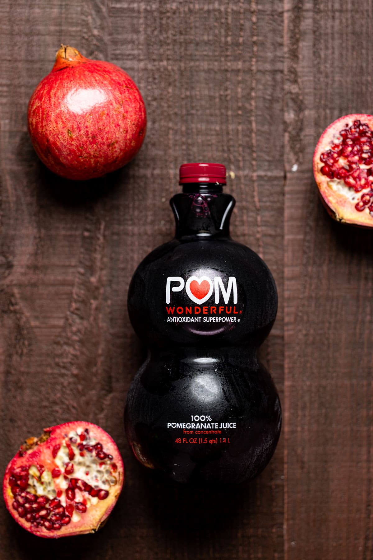 Bottle of POM pomegranate juice next to two pomegranate halves and one full pomegranate