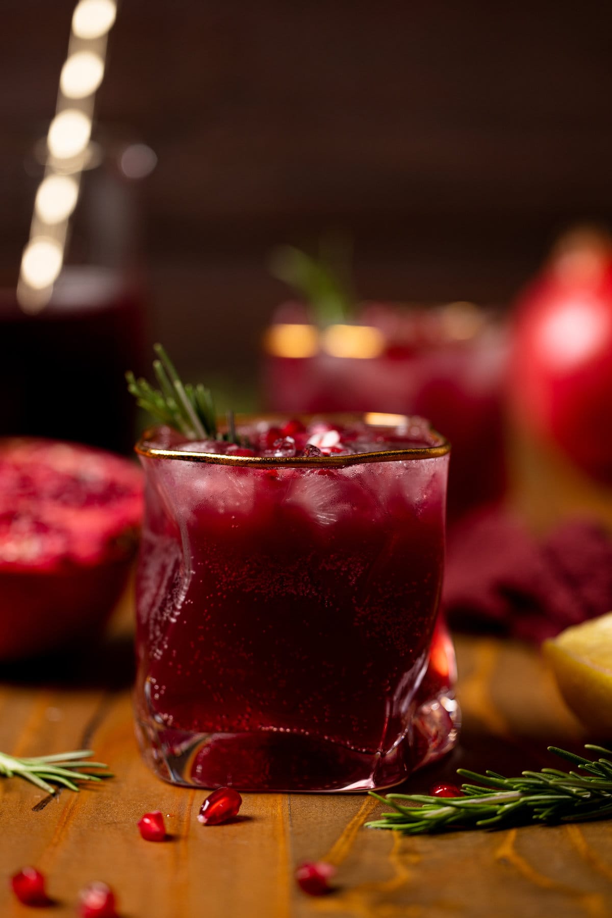 Holiday Pomegranate Ginger Mocktail in a gold-rimmed glass garnished with rosemary and pomegranate seeds