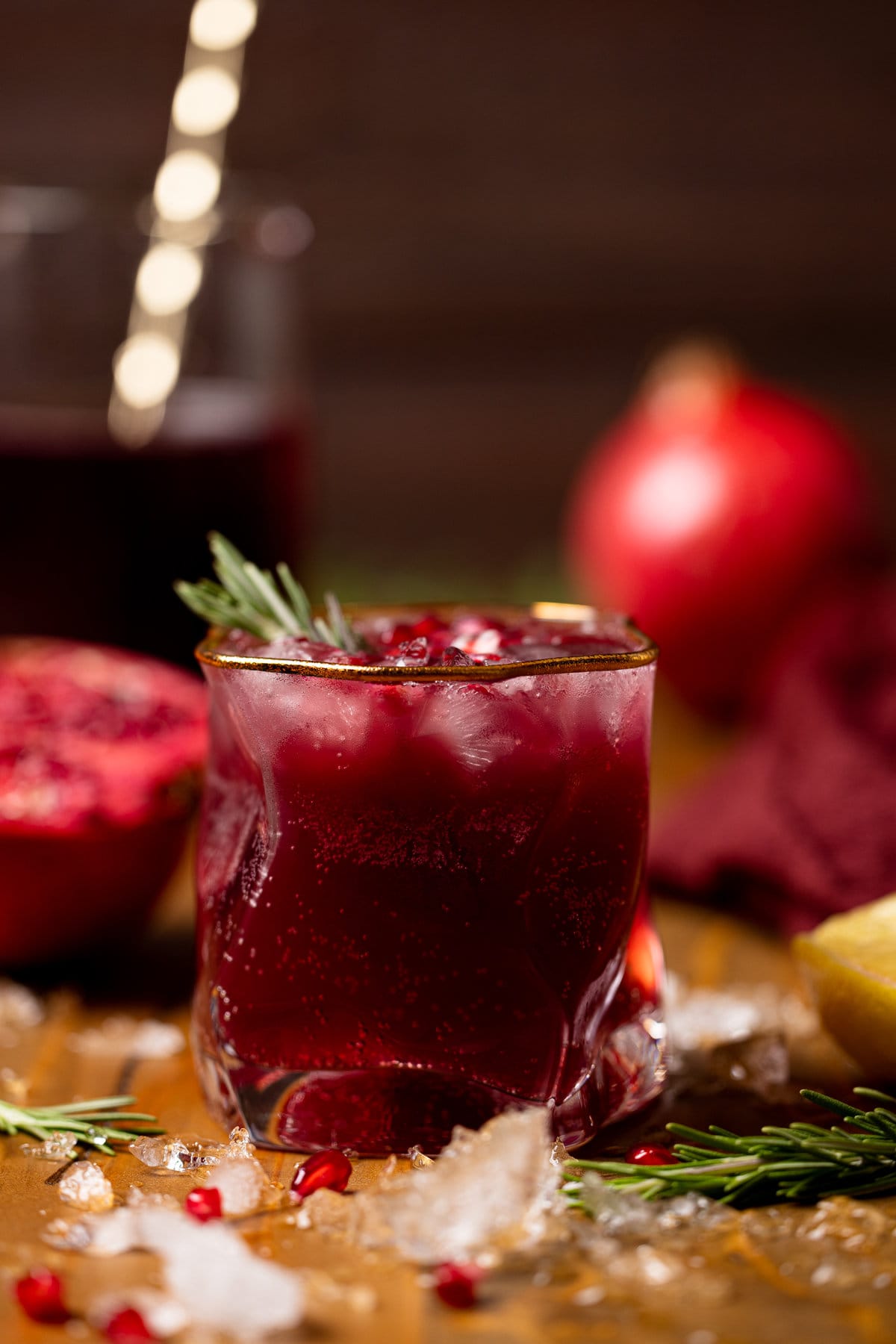 Holiday Pomegranate Ginger Mocktail in a gold-rimmed glass garnished with rosemary and pomegranate seeds