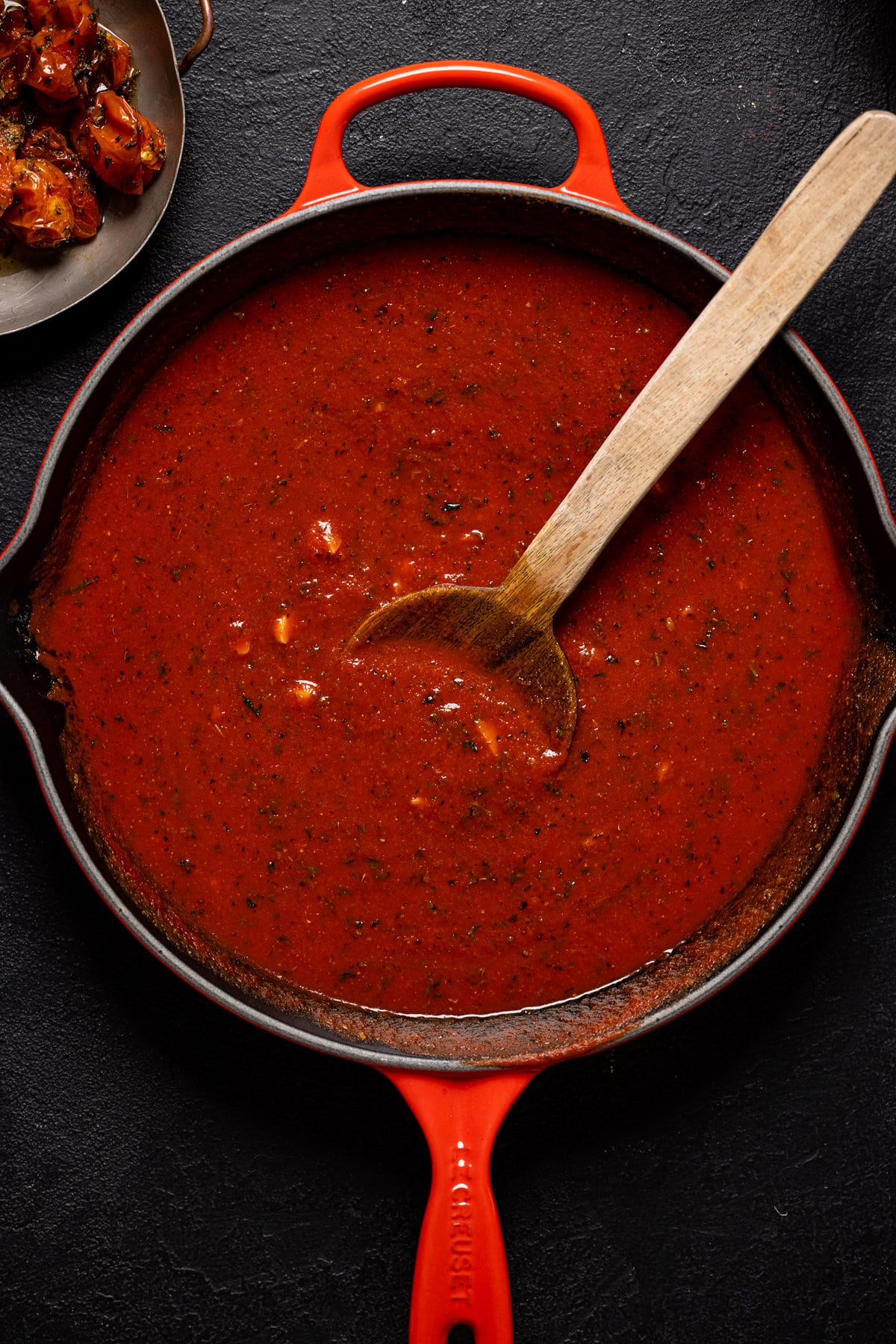 Wooden spoon stirring a pan of tomato sauce