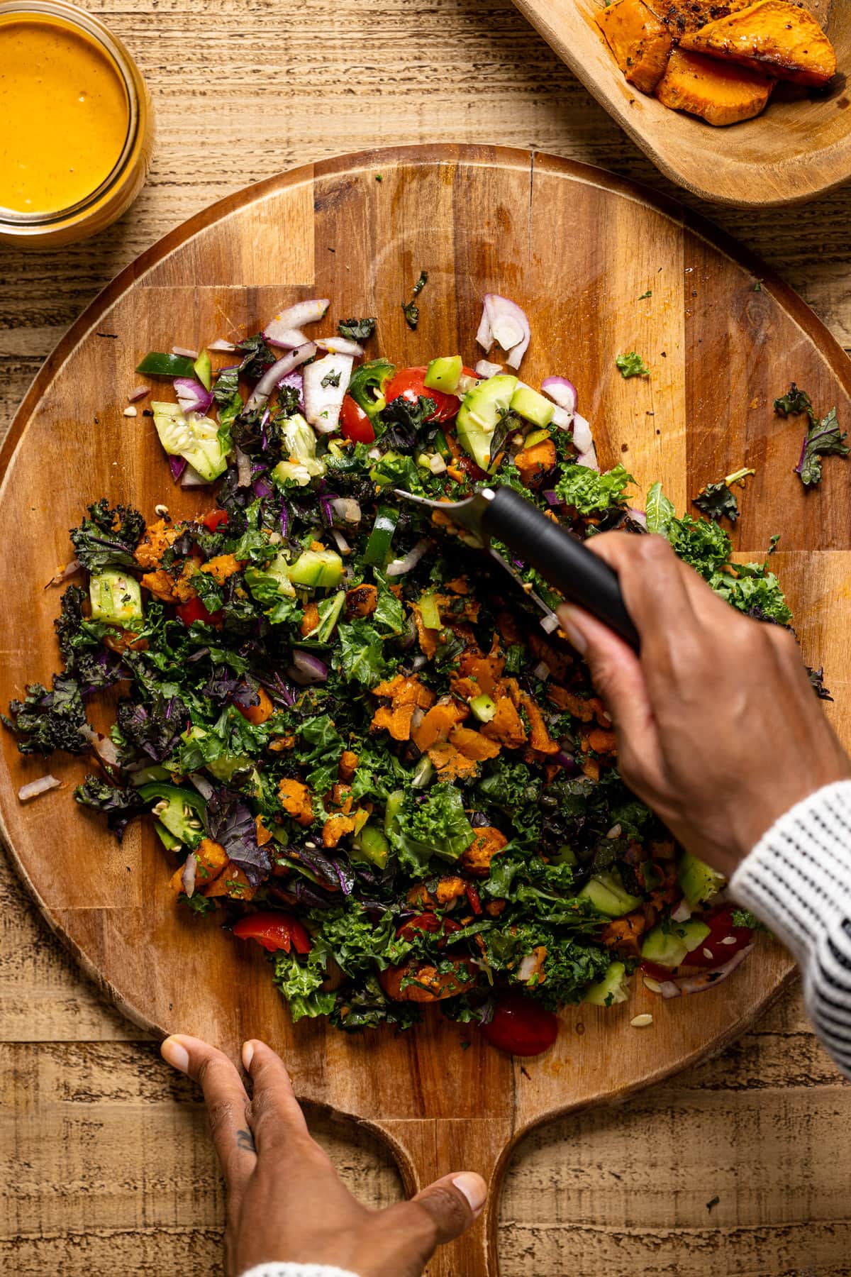 Hand with a knife chopping colorful ingredients on a large wooden cutting board