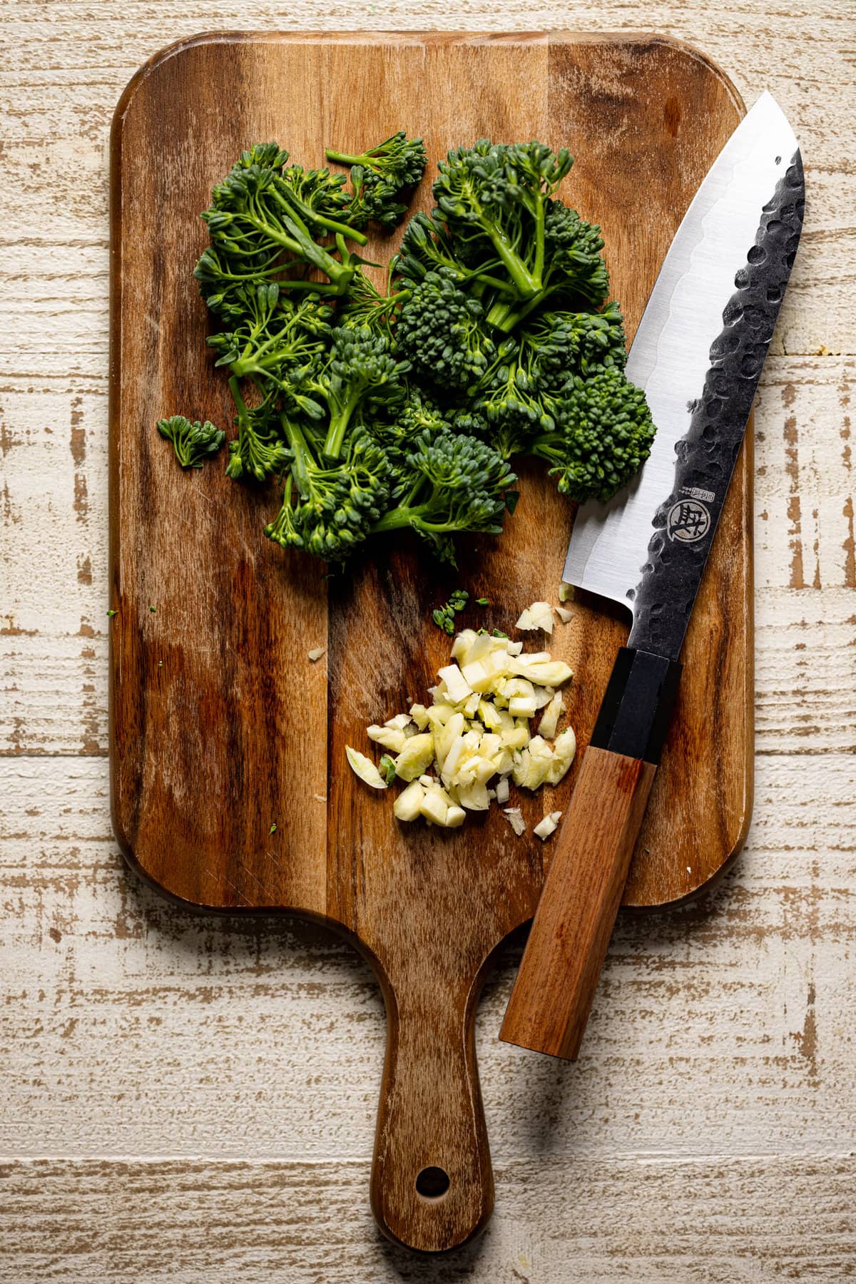 Chopped broccoli and garlic on a cutting board with a knife