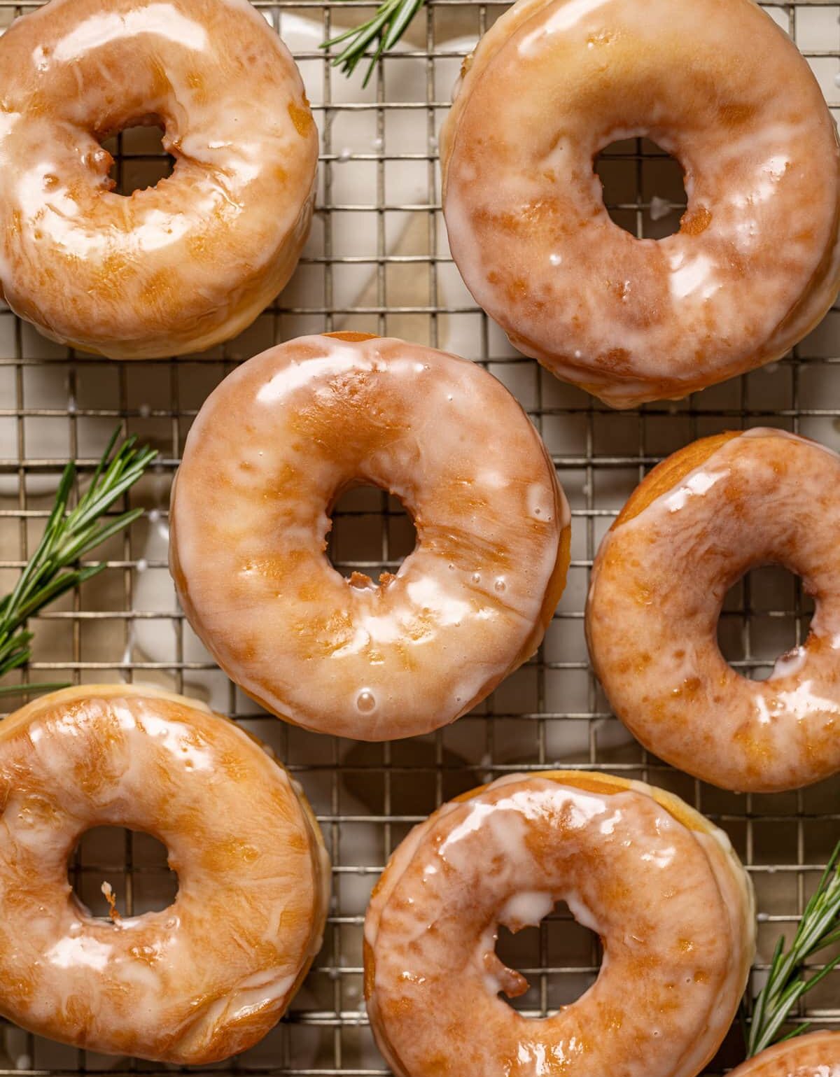 Glazed doughnuts on a wire rack with a rosemary garnish. 