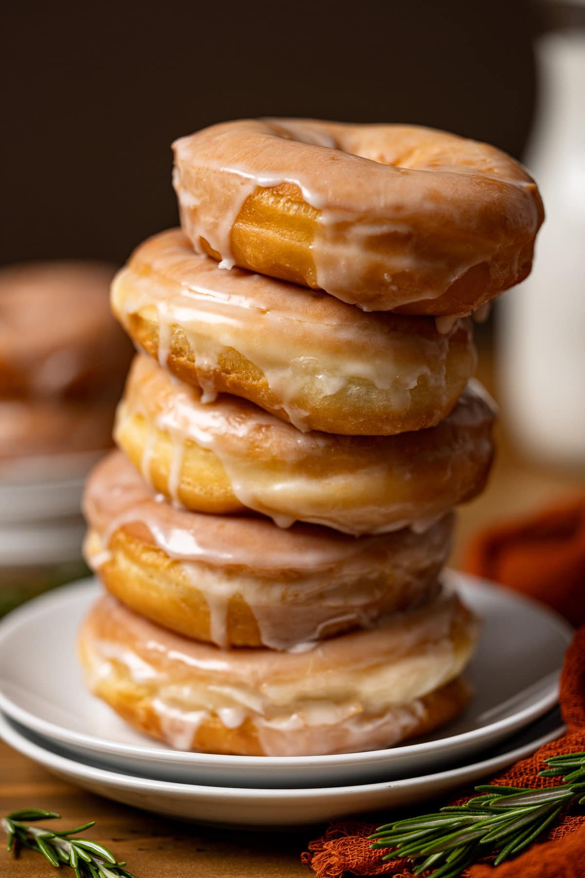 Up close shot of doughnuts stacked on two plates with a dark brown background with a red napkin and rosemary garnish.