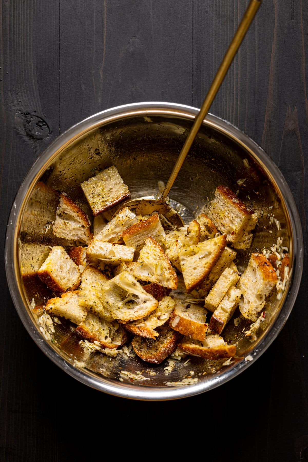 Bread pieces being stirred with seasonings in a bowl