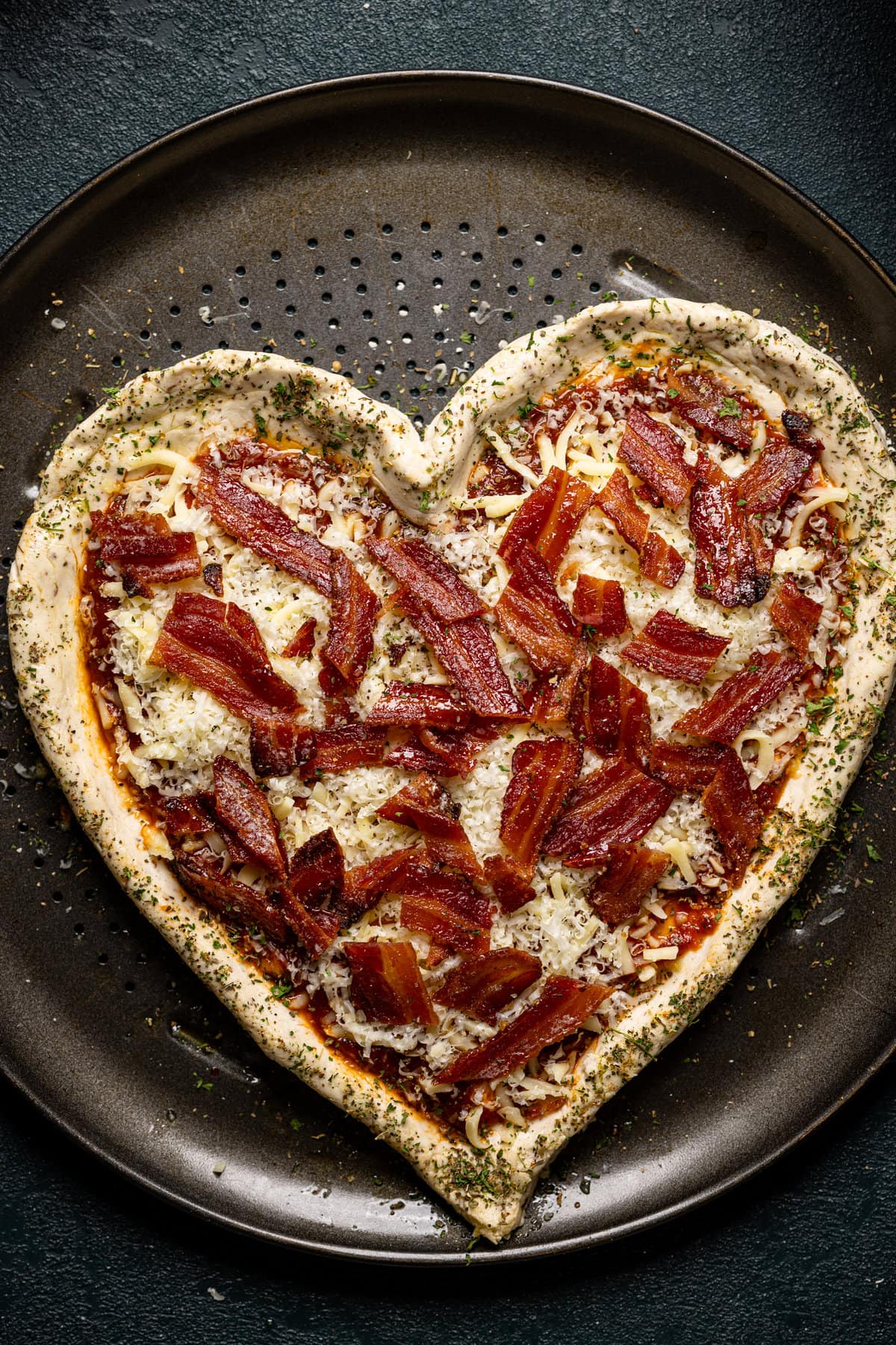 Uncooked heart-shaped Gluten-Free Hot Honey Bacon Pizza on a pan