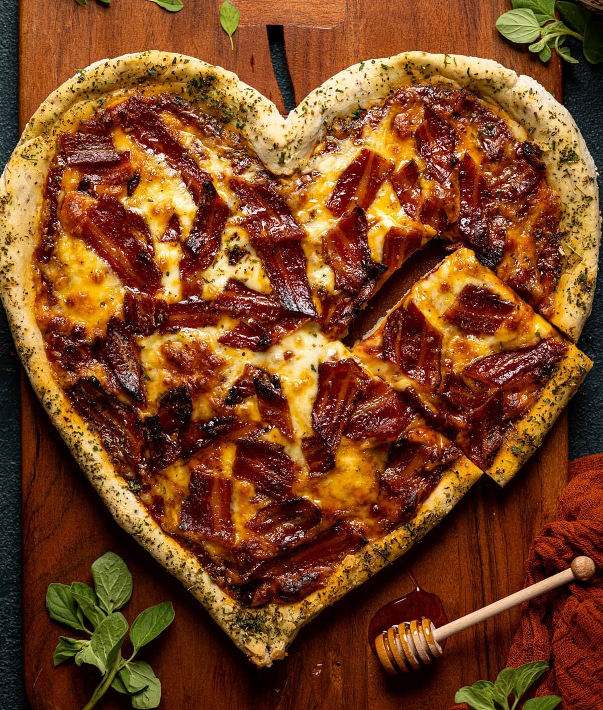 Overhead shot of heart-shaped Gluten-Free Hot Honey Bacon Pizza with a piece cut out