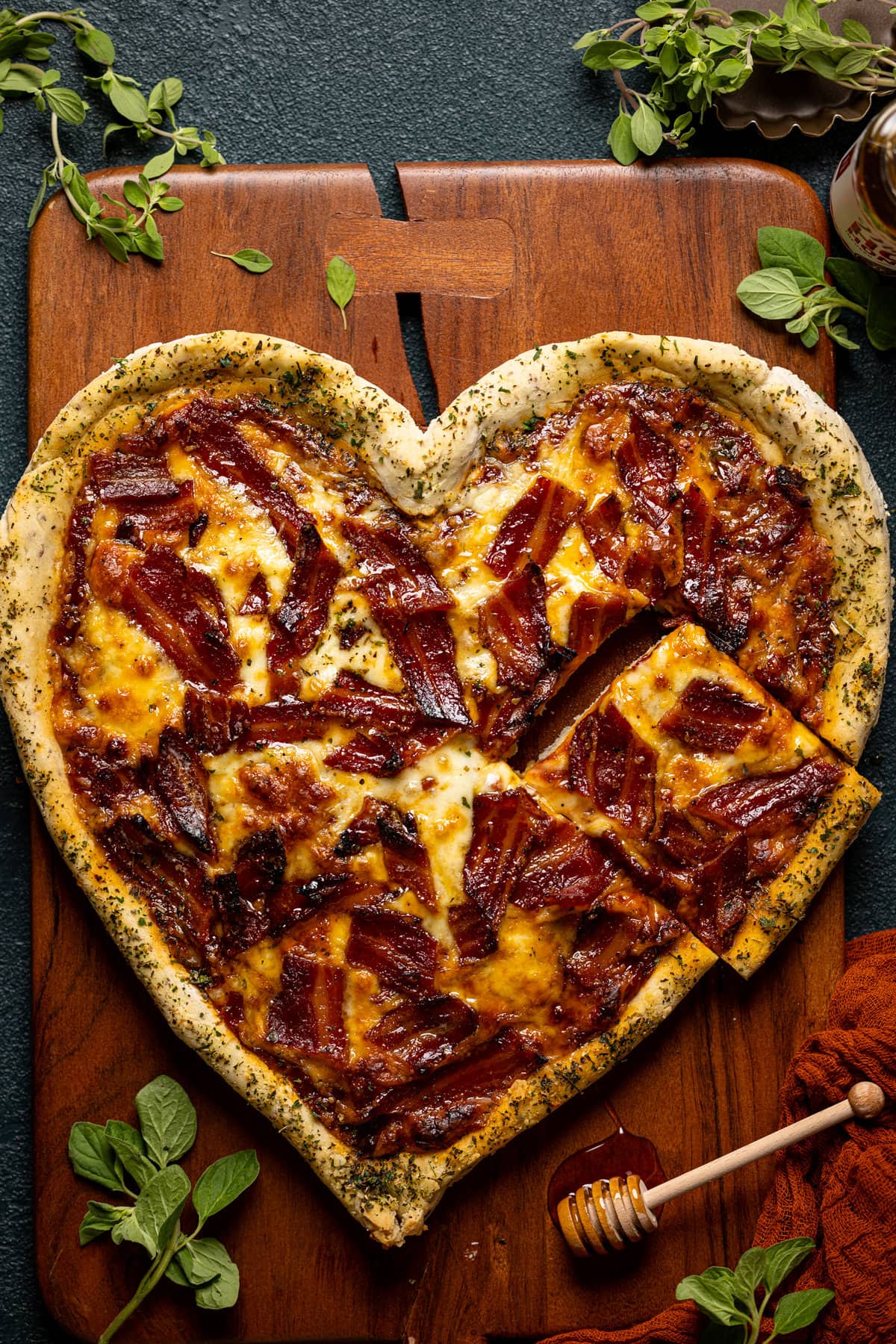 Overhead shot of heart-shaped Gluten-Free Hot Honey Bacon Pizza with a piece cut out