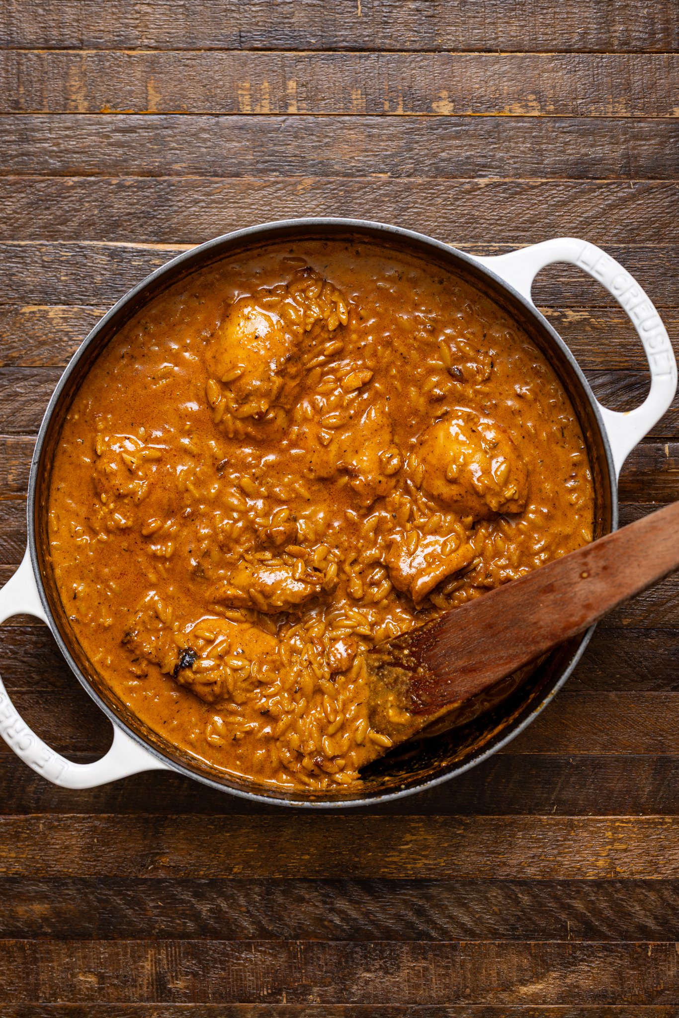 One Pot Creamy Cajun Chicken Orzo in a white skillet with a wooden spoon.