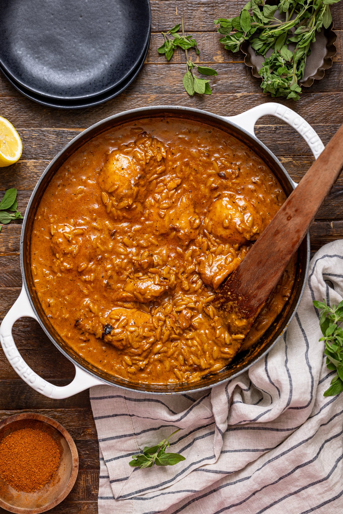 One Pot Creamy Cajun Chicken Orzo in a deep skillet with a wooden spoon with plates.
