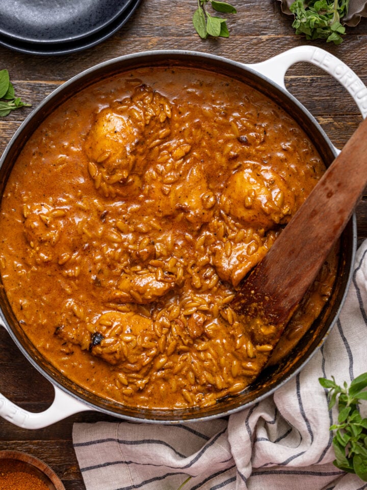One Pot Creamy Cajun Chicken Orzo in a deep skillet with a wooden spoon with a drink and plates.