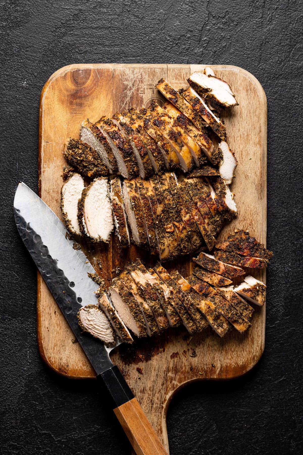 Seasoned and sliced chicken on a cutting board with a knife