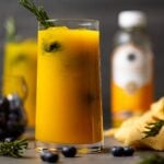 Glass of Mango Lemonade Kombucha Mocktail with a sprig of rosemary