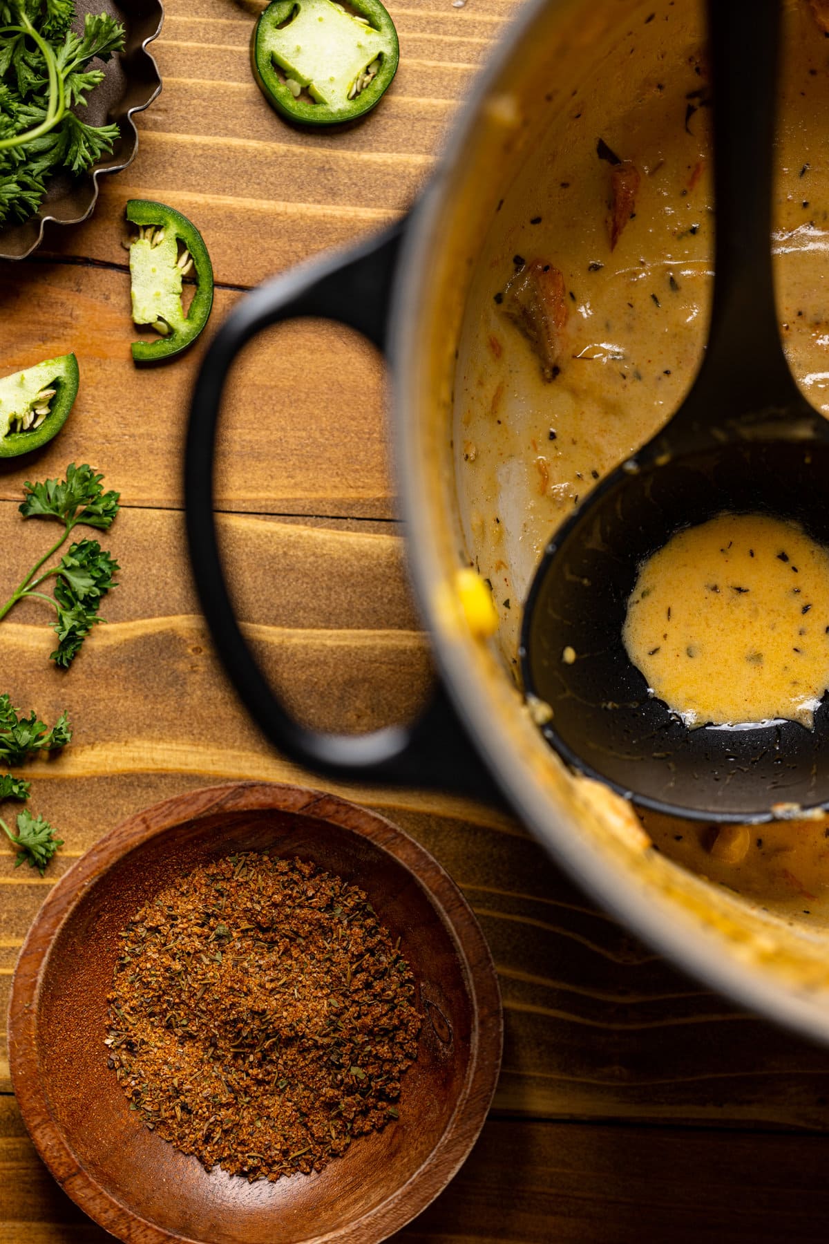 Wooden bowl of spices next to an almost-empty pot of creamy blackened salmon chowder