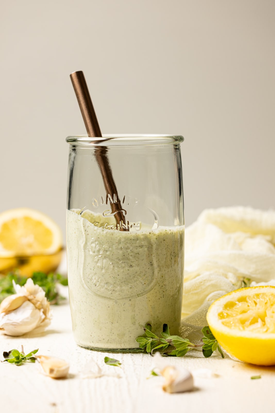 Lemon garlic dressing in a mason jar with a spoon on a white table. 