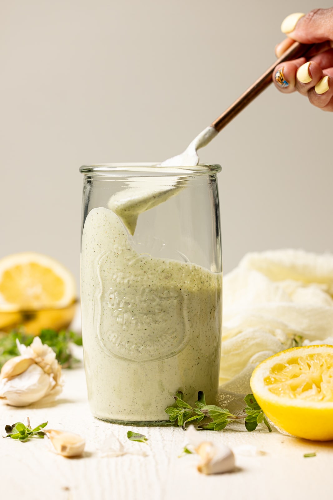 Lemon garlic dressing in a mason jar being scooped up using a spoon on a white table.