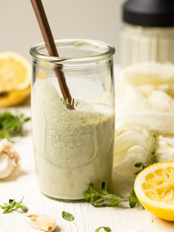 Lemon garlic dressing in a mason jar with a spoon on a white table.
